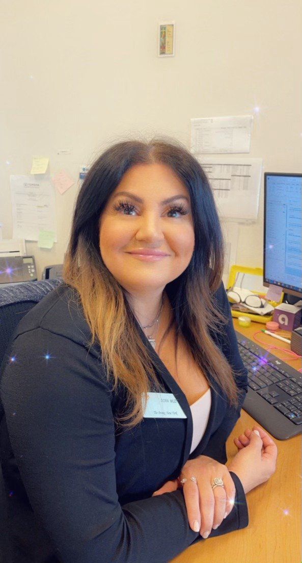 Woman in black jacket, smiling at a desk with a computer and keyboard.