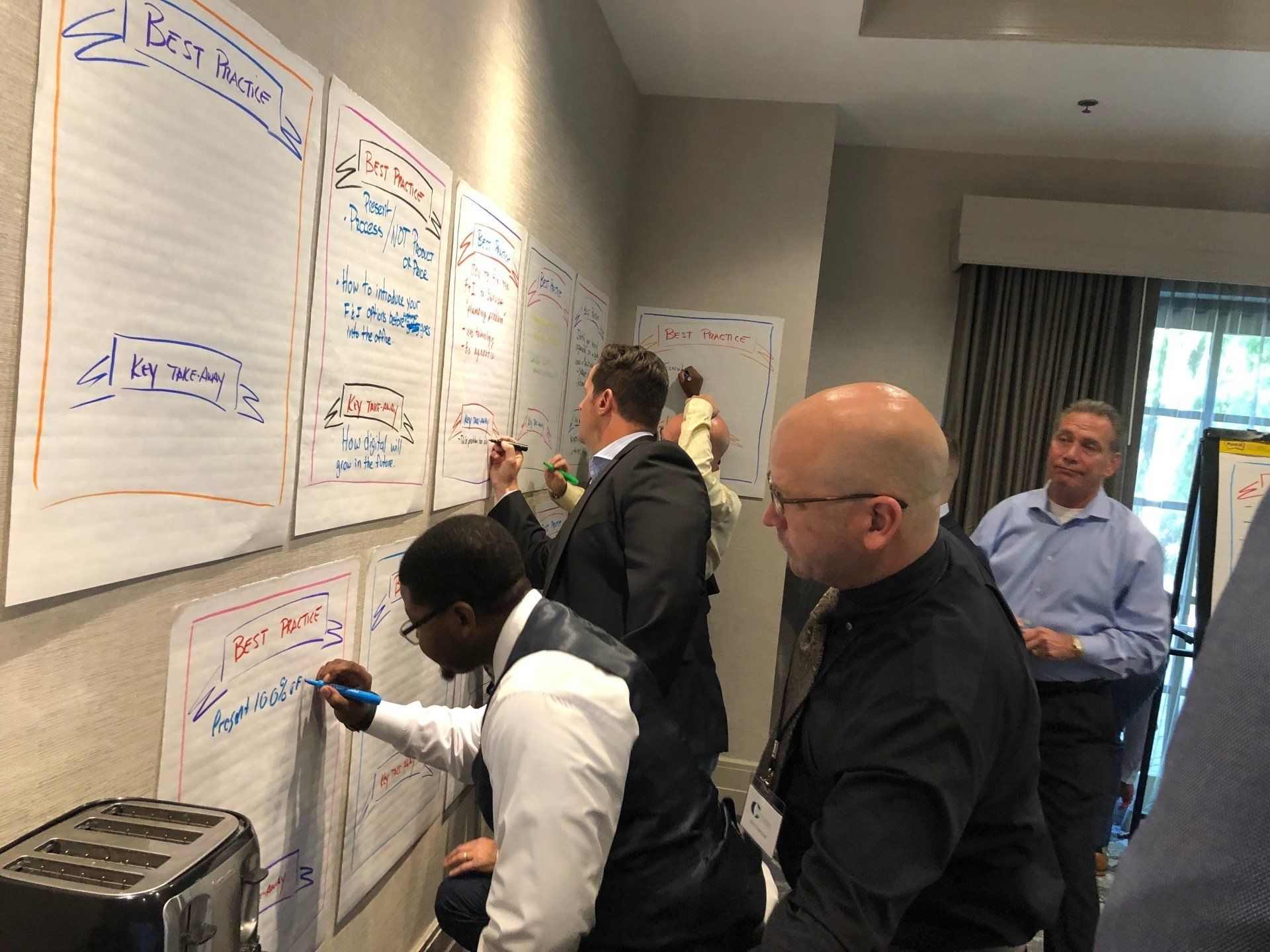 A group of men are writing on a whiteboard in a room.