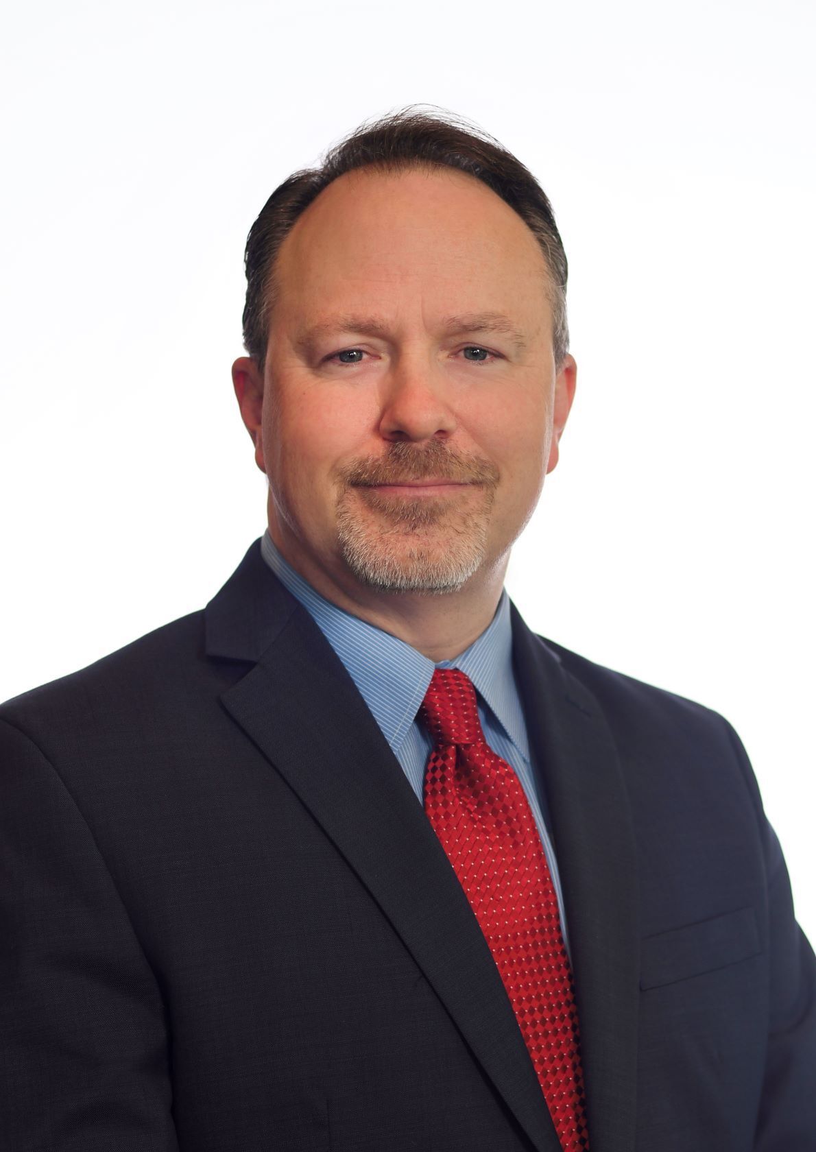 Man in suit and red tie, smiling, against a white backdrop.