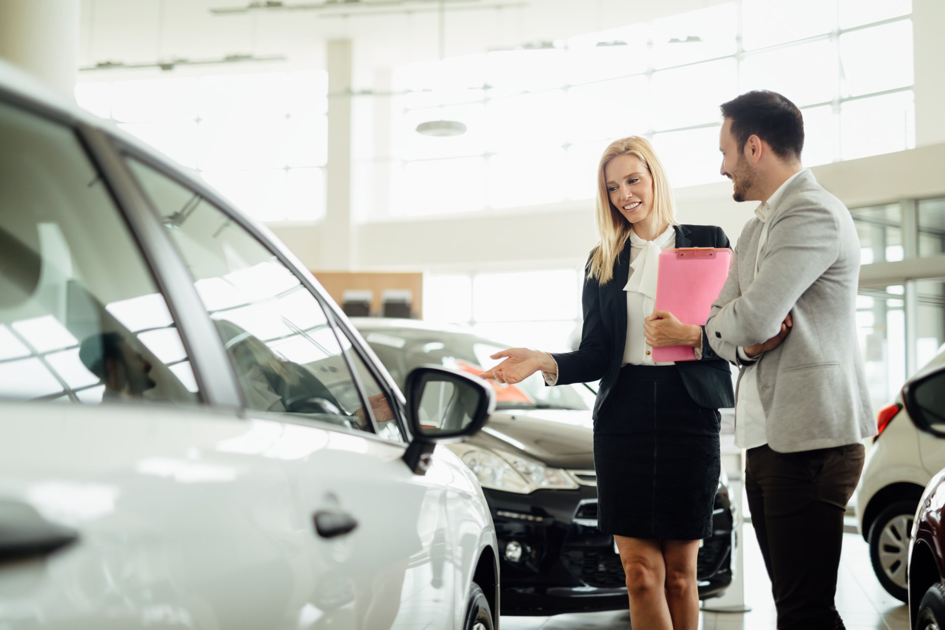 Car salesperson showing a customer a white car in a dealership.