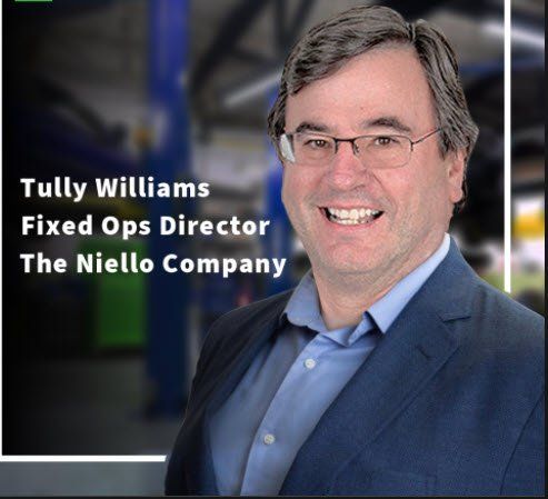 Tully Williams, Fixed Ops Director, smiles in a dark suit. Background of a car shop.