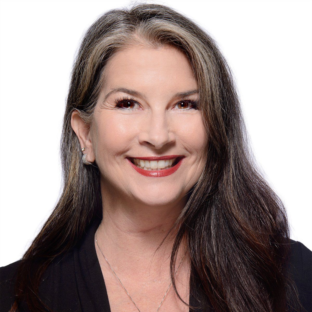 Woman with long brown and gray hair smiles, wearing a black blazer and necklace.