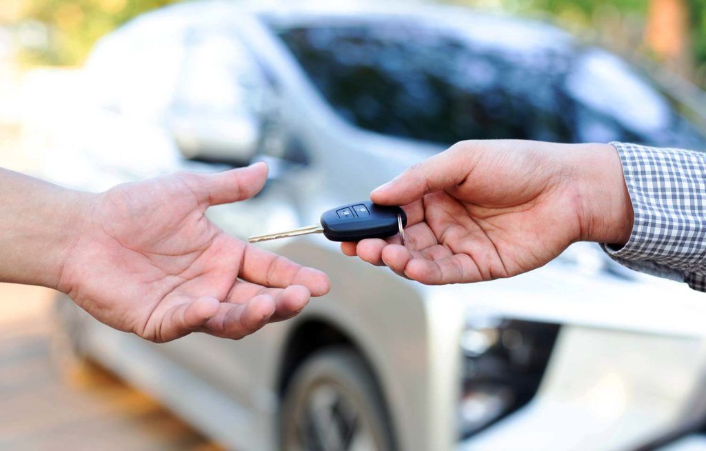Hands exchanging car keys in front of a silver car.