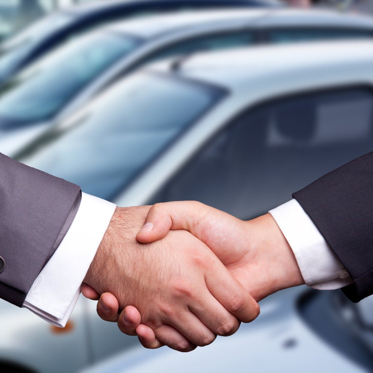 Two people shaking hands in front of a row of silver cars, signifying a car sale.