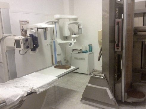 Sala radiologica dell'ospedale con apparecchio di imaging, lettino per esami e pannello di controllo.