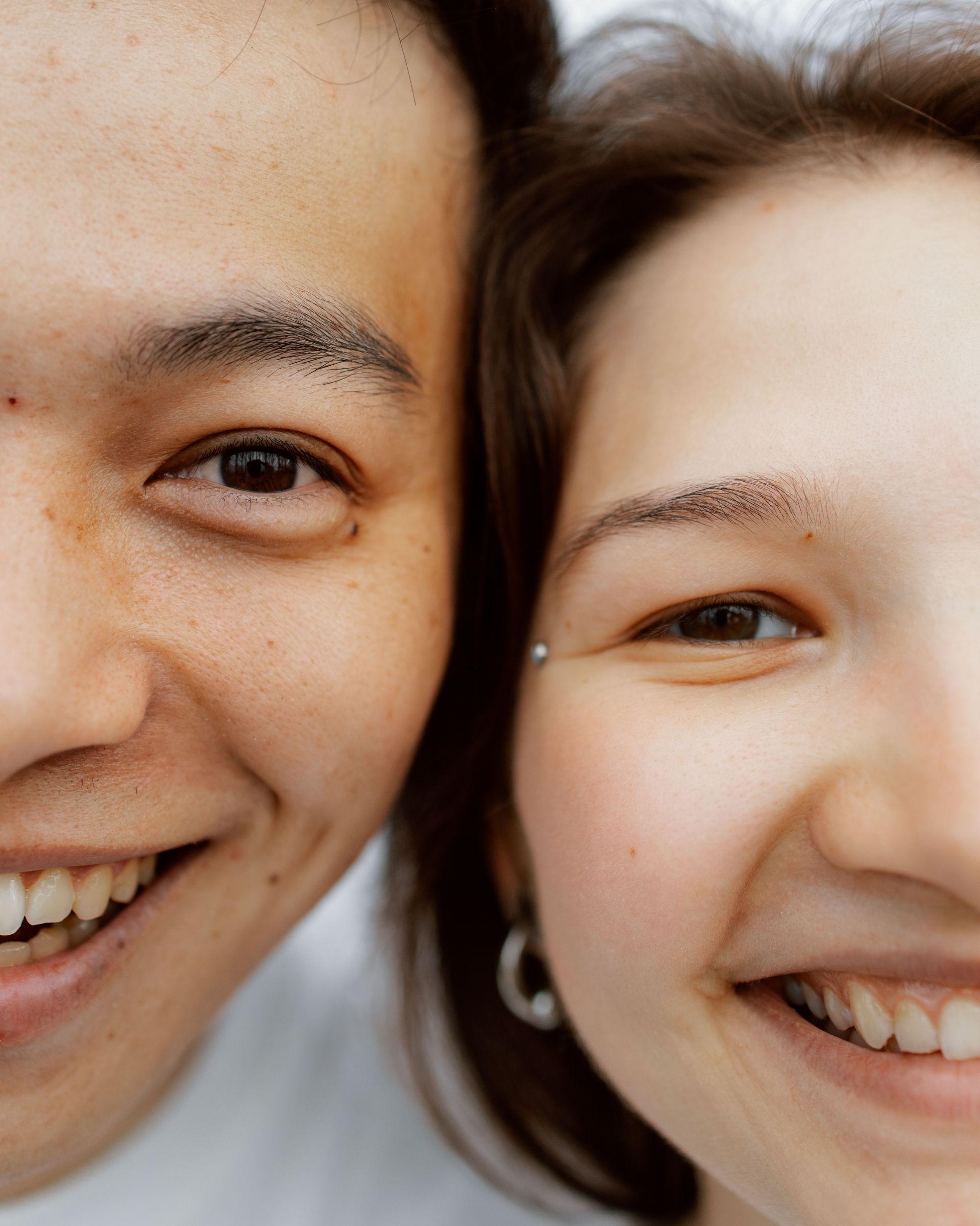 Two smiling faces close together, one in a white top and one with a small hoop earring