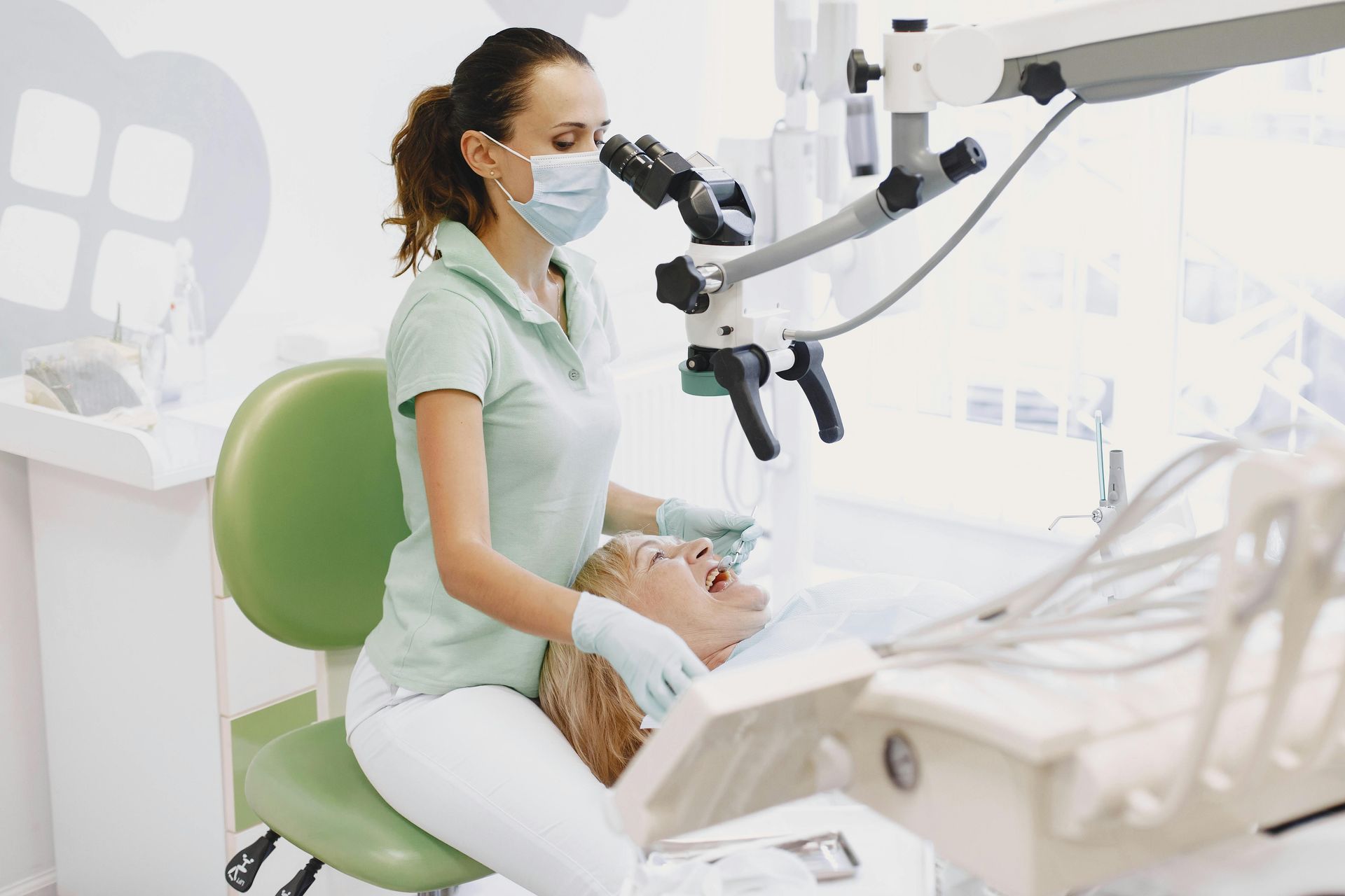 Dentist examining a patient in a bright dental clinic with a microscope and green chair