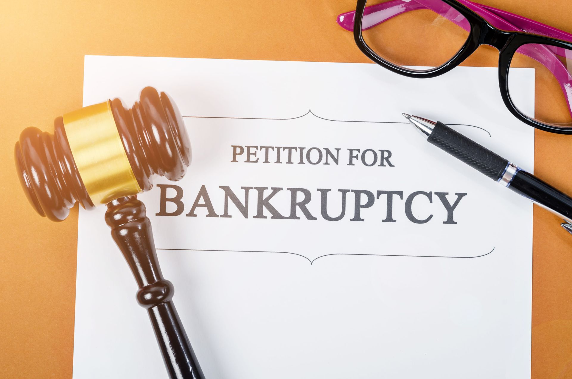 Bankruptcy petition document with judge's gavel, pen, and glasses on a desk