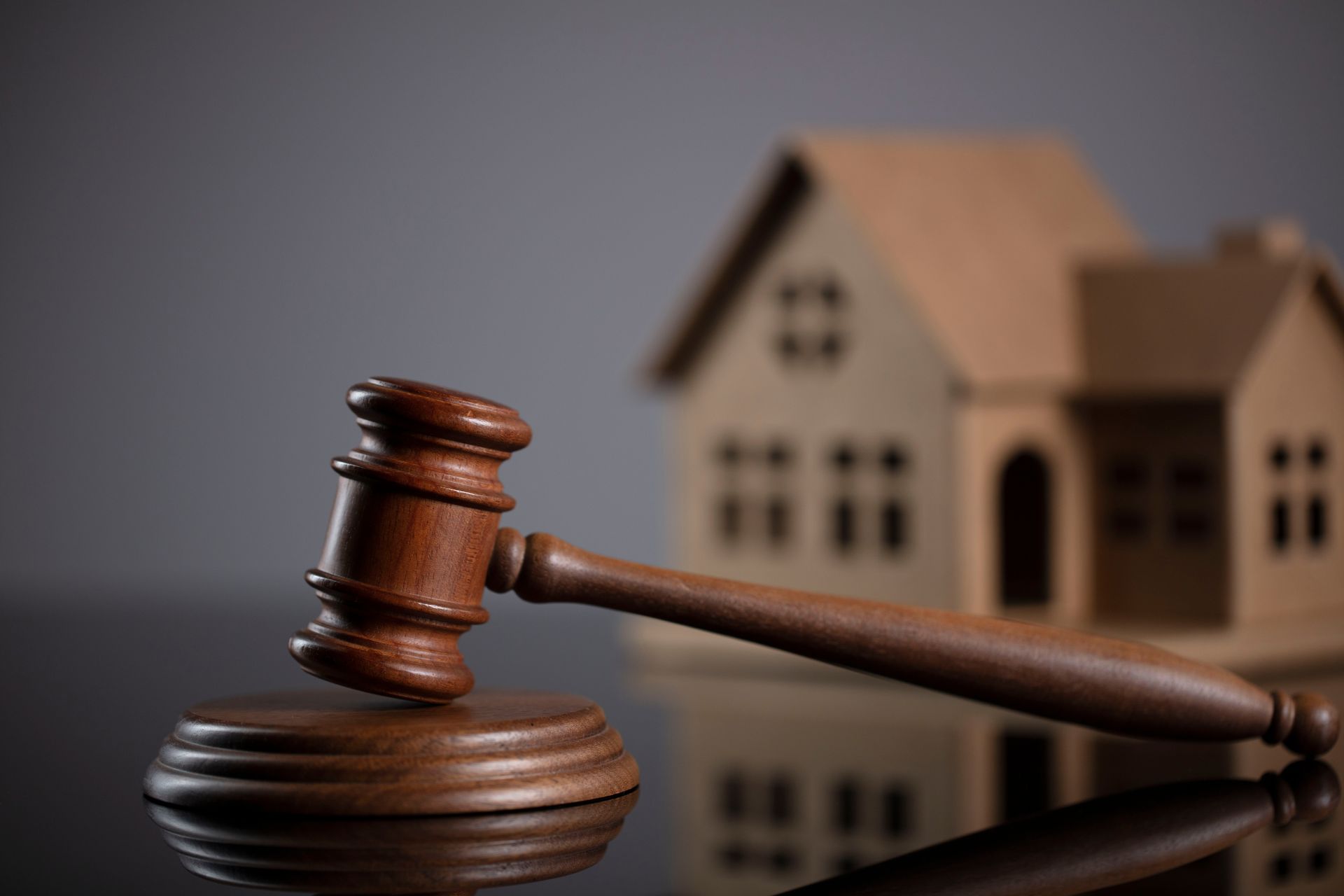 Wooden gavel and house model on reflective surface.