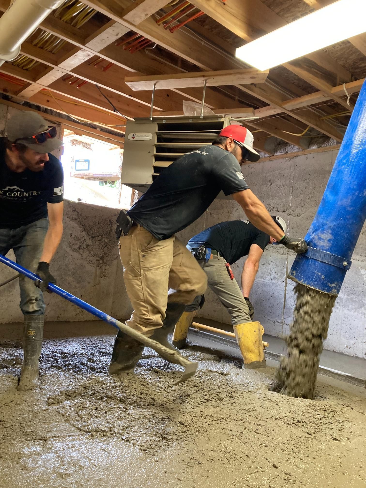 Two men are pouring concrete into a basement.