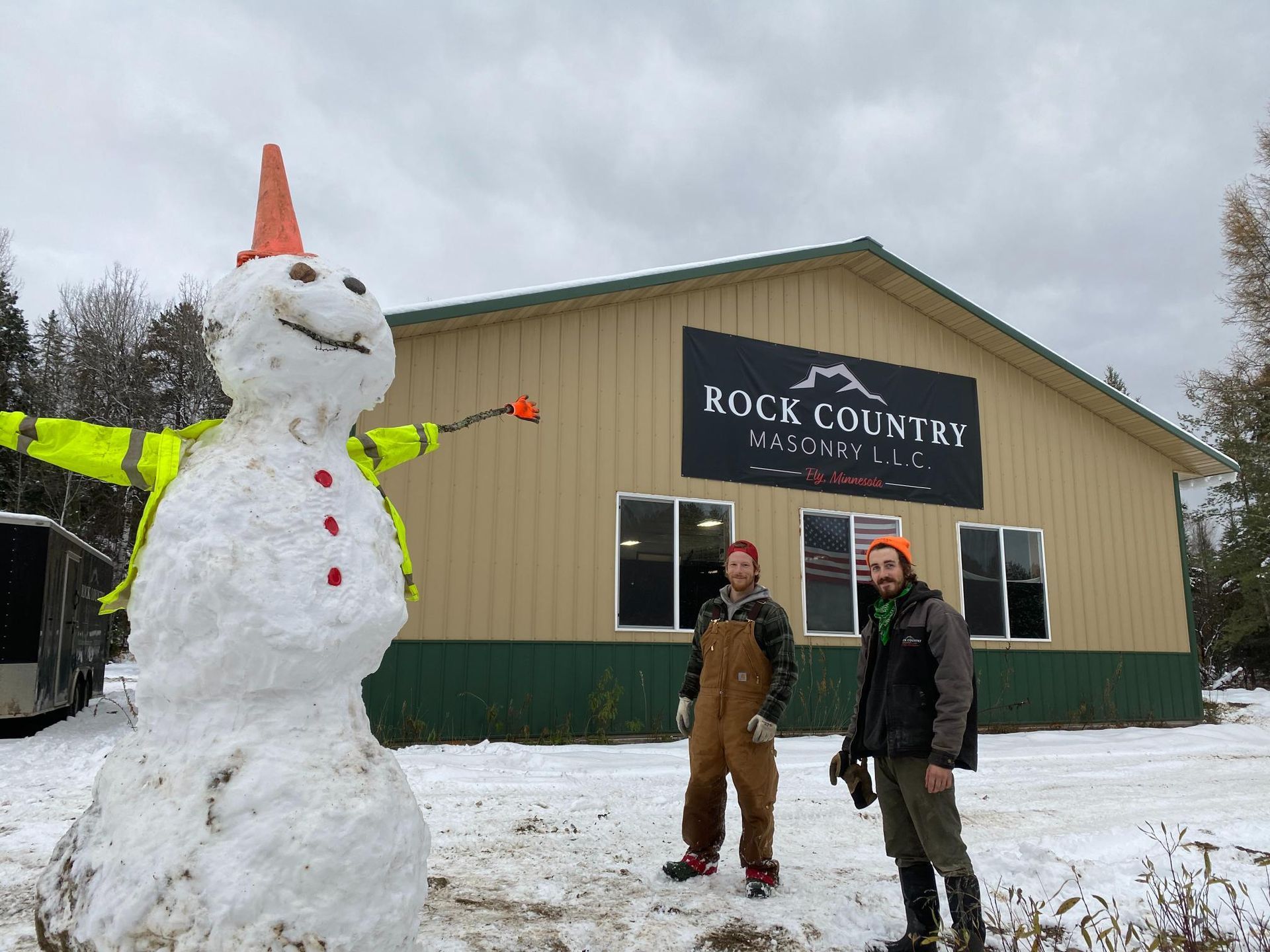 Two men are standing next to a snowman in front of a building.