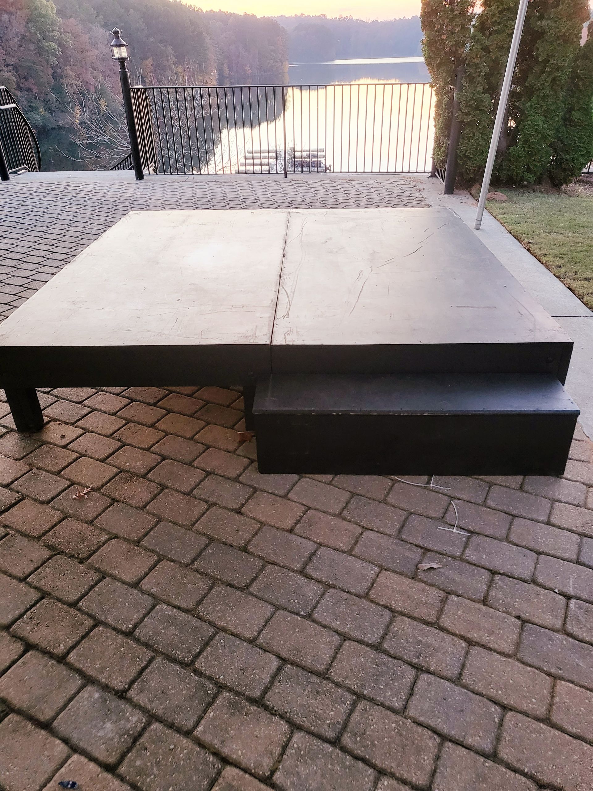 A large black table is sitting on a brick patio next to a lake.