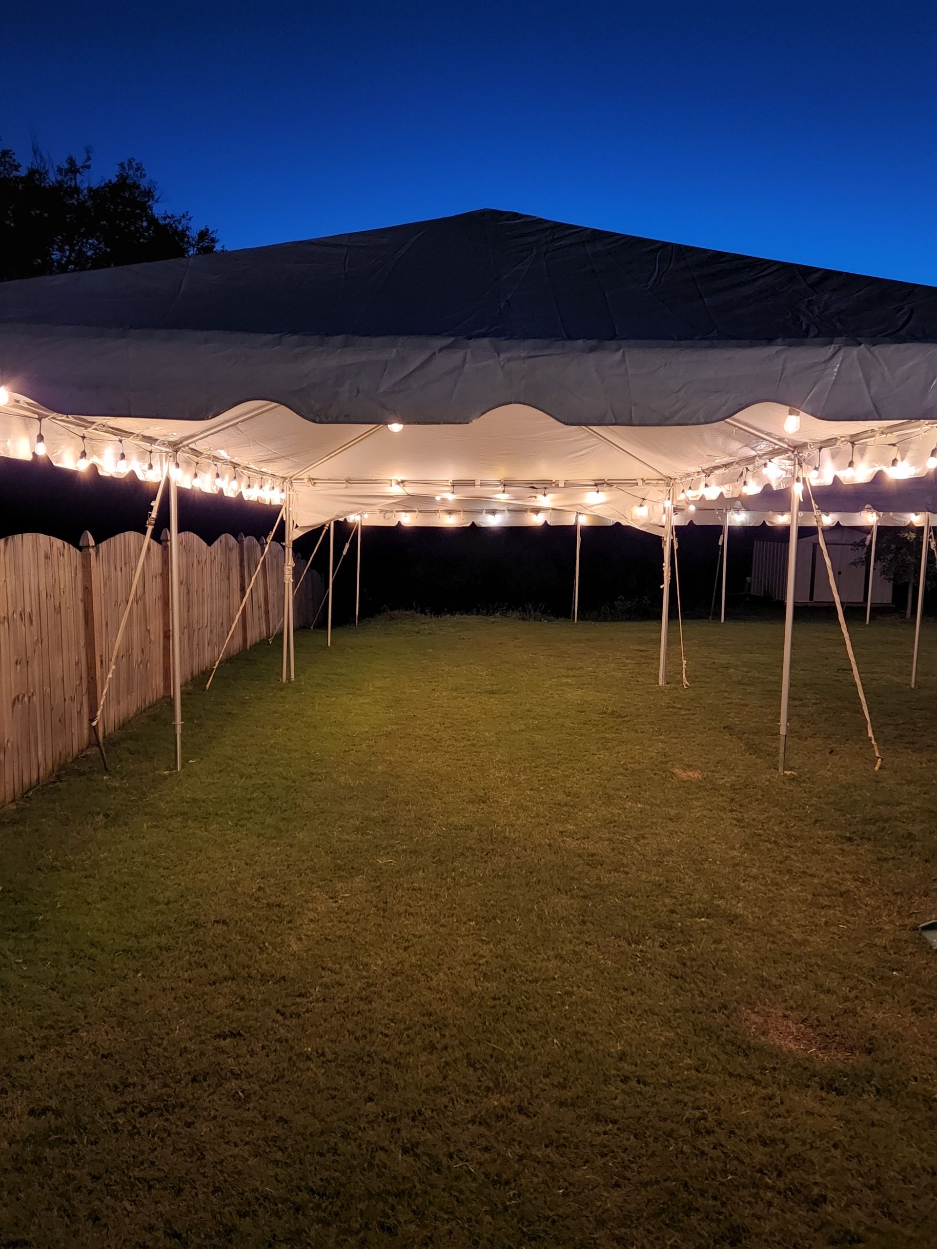 A large white tent is lit up at night in a backyard.