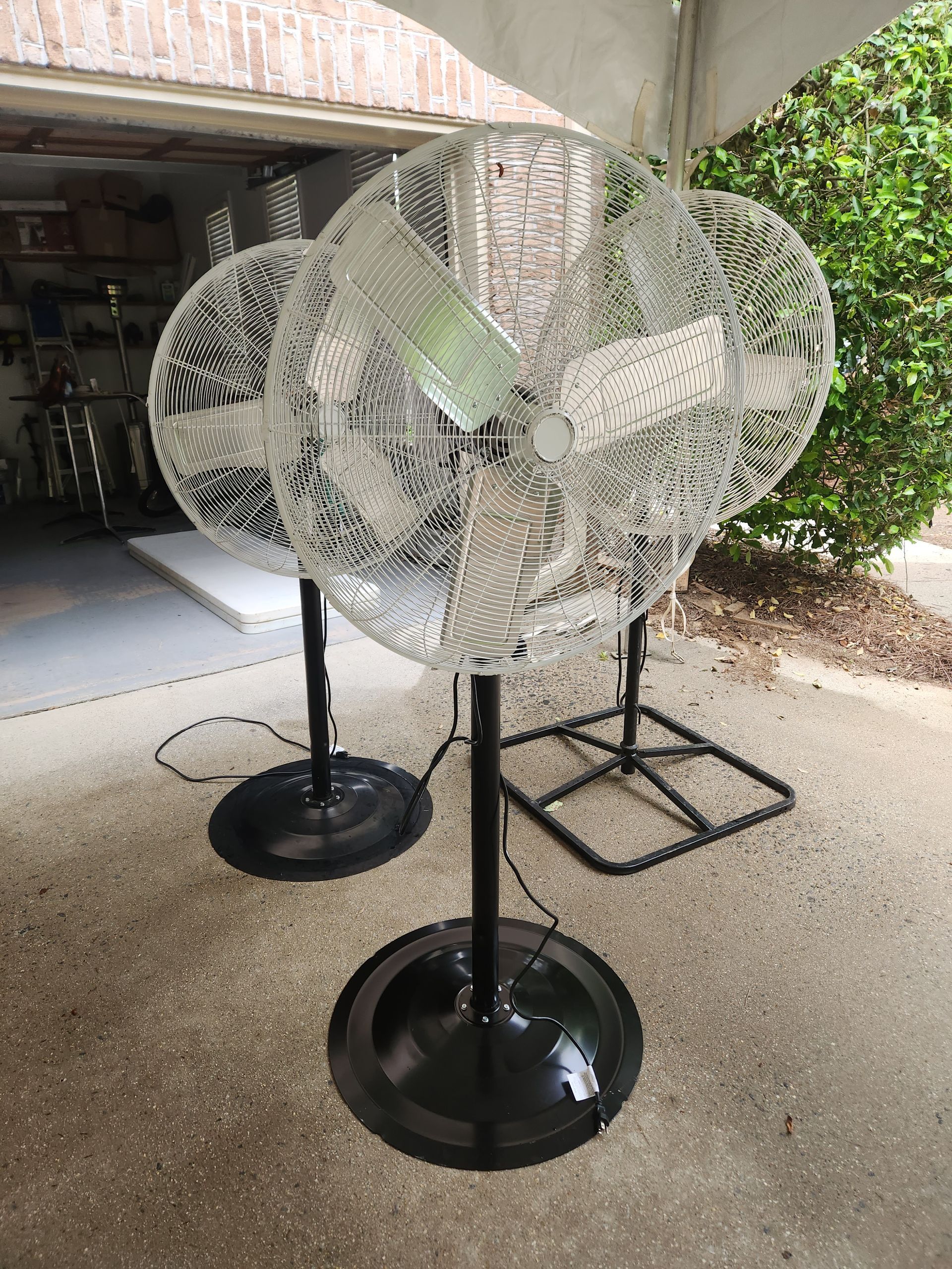 A large white fan is sitting in the grass in front of a wooden fence