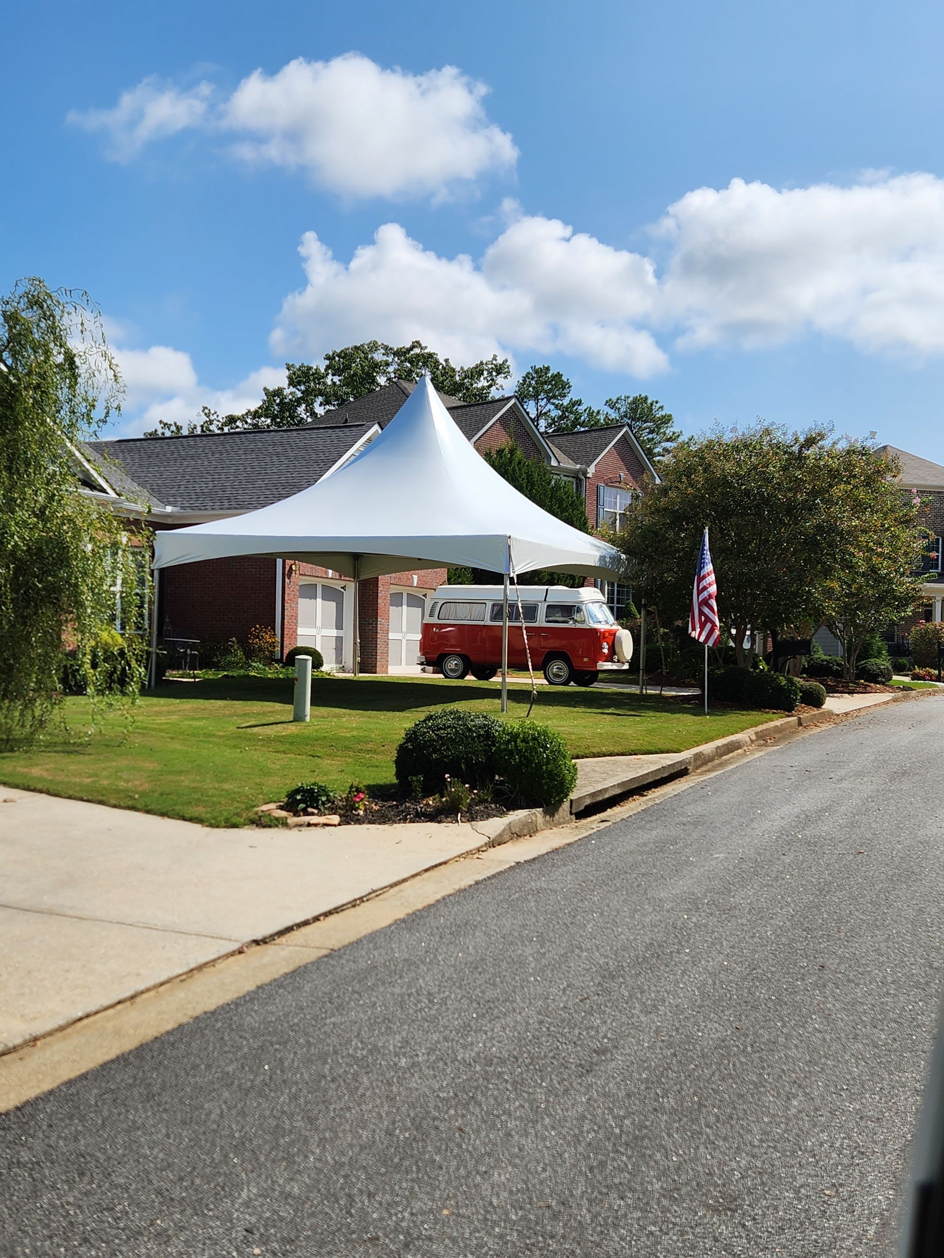 A red van is parked under a white tent in front of a house