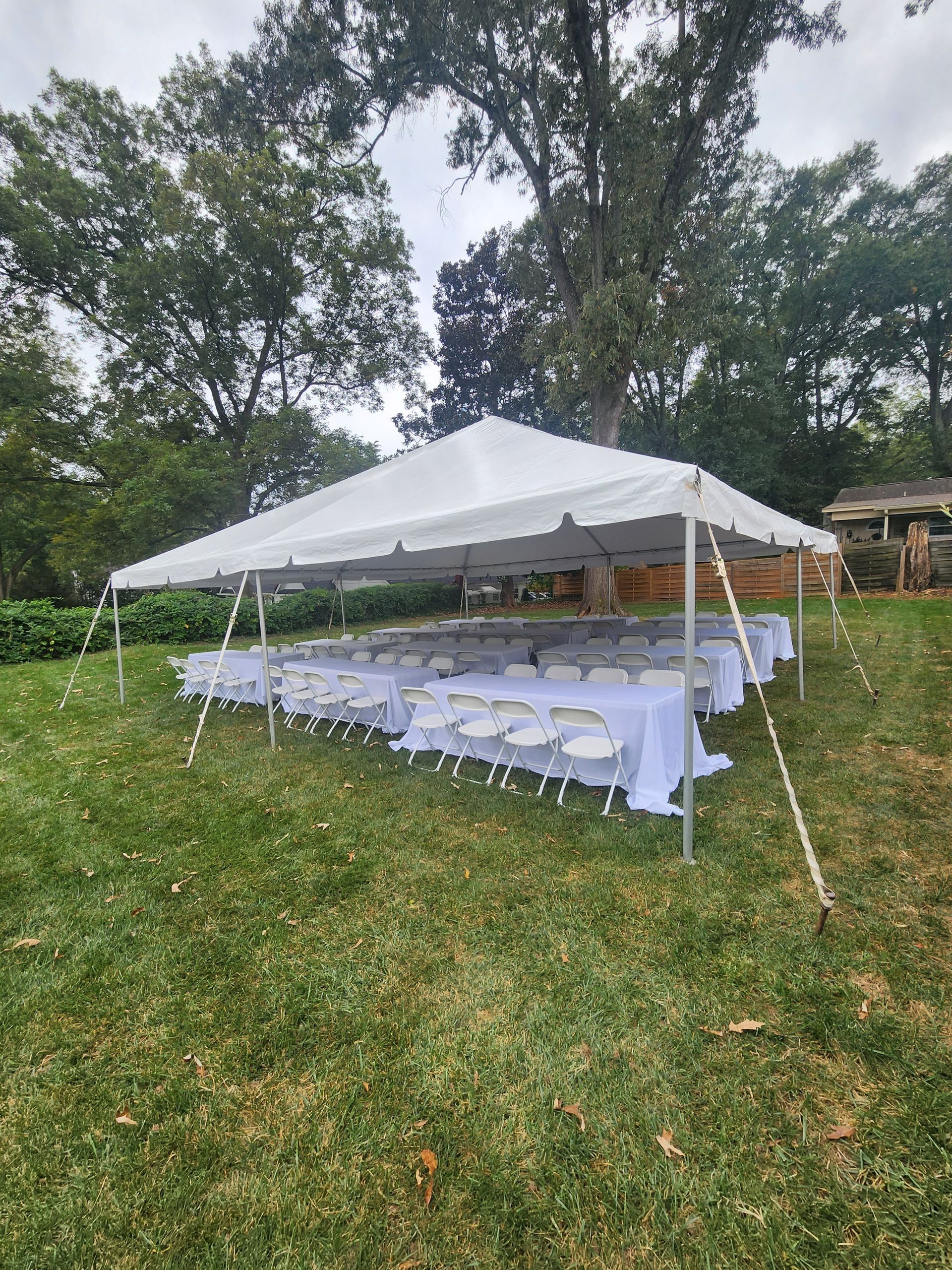 A large white tent with tables and chairs underneath it in a grassy field.
