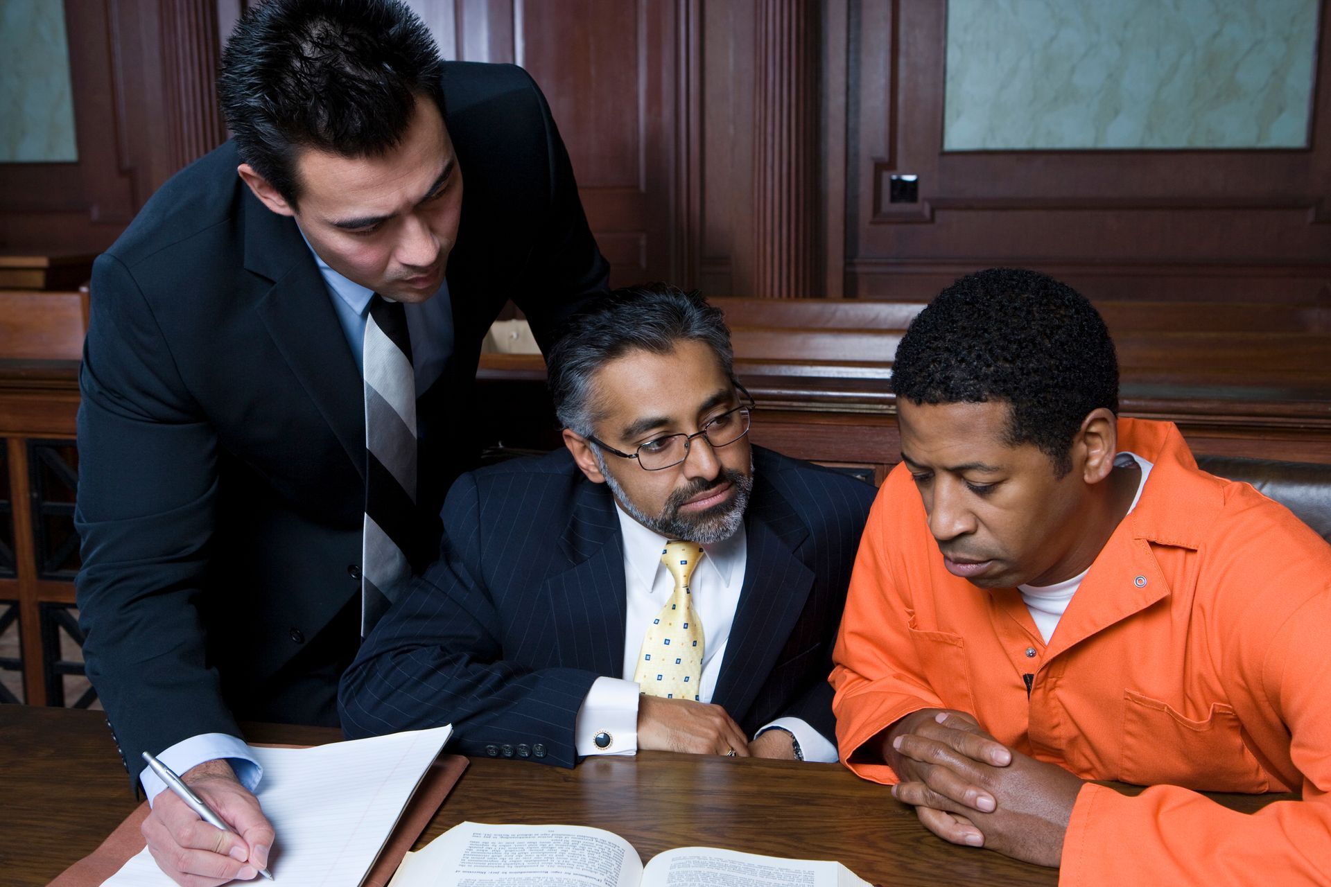 Attorney and client in orange jail uniform reviewing documents in a courtroom setting. Attorney and client in orange jail uniform reviewing documents in a courtroom setting.