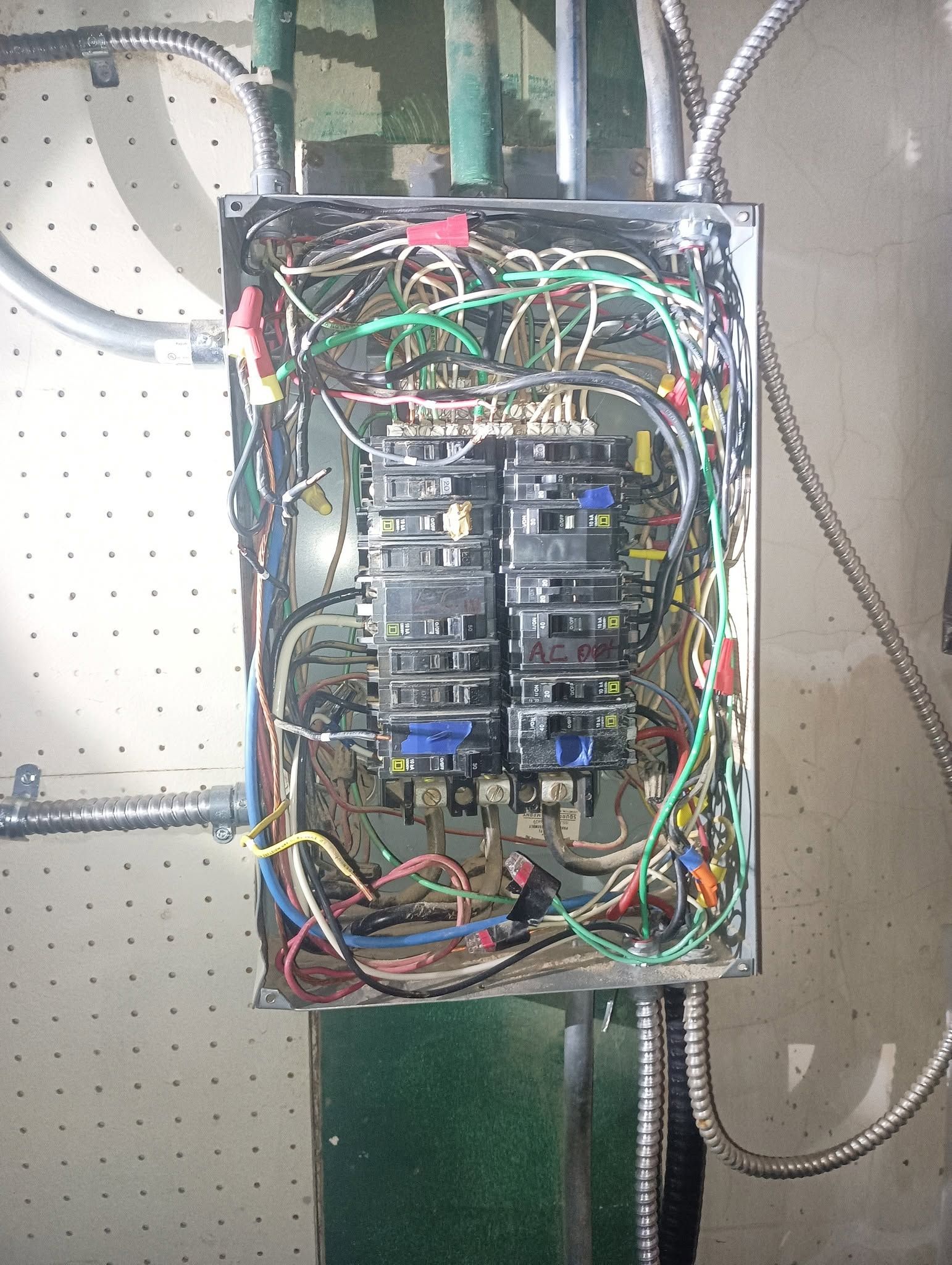 Open electrical breaker panel with tangled multicolored wires on a pegboard wall