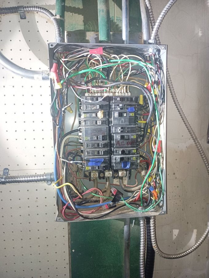 Open electrical breaker panel with tangled multicolored wires on a pegboard wall