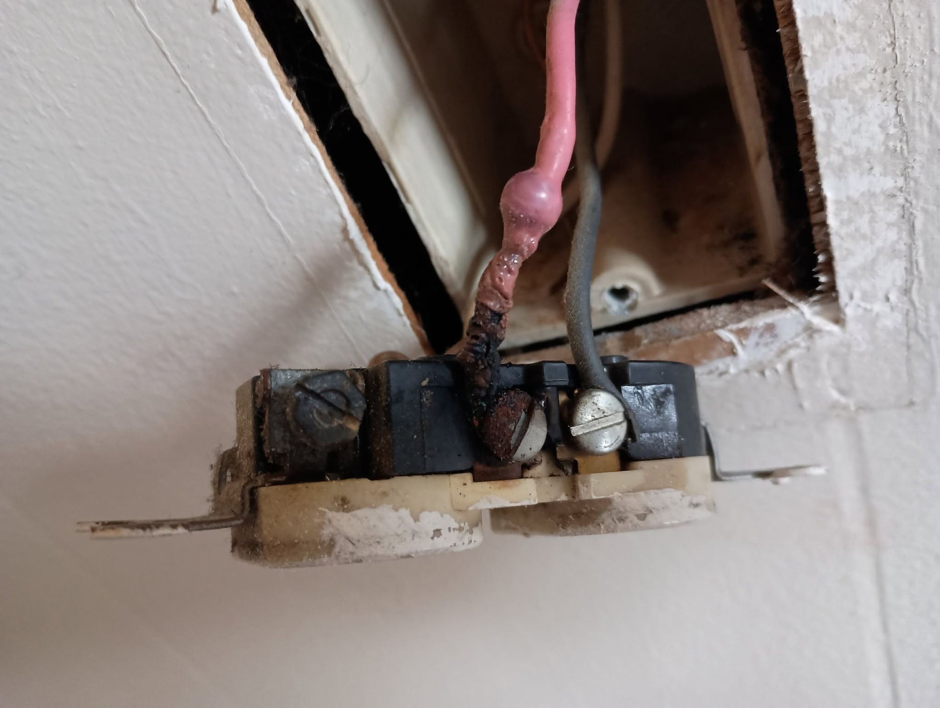 Exposed electrical outlet wiring with a loose red cable and damaged wall opening
