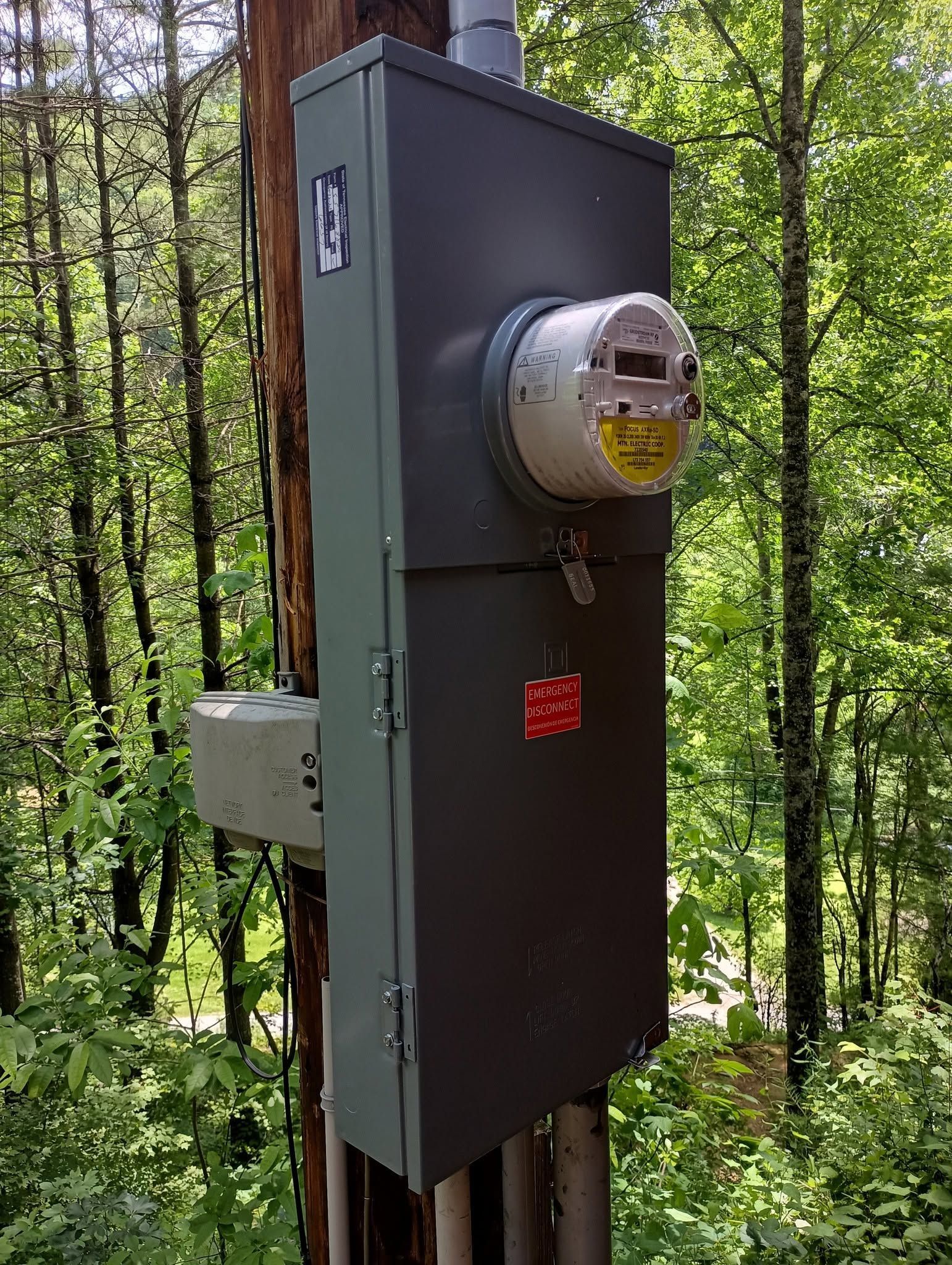 Outdoor electric meter box mounted on a dark panel in a wooded area