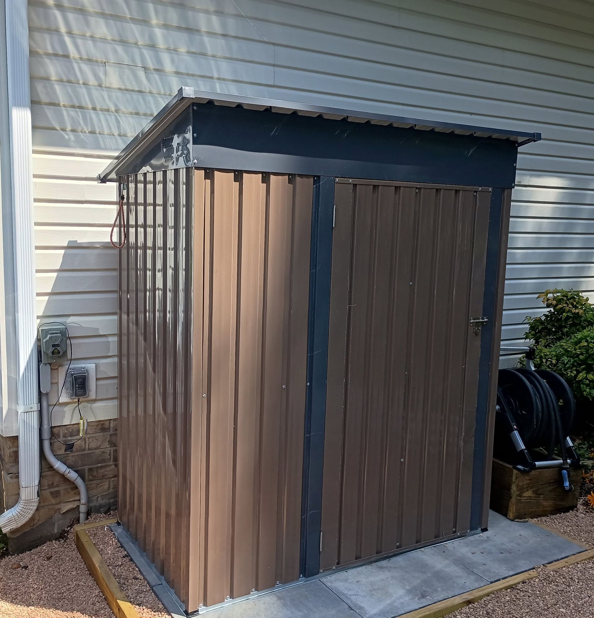 Brown outdoor storage shed with a dark roof beside a house in a backyard