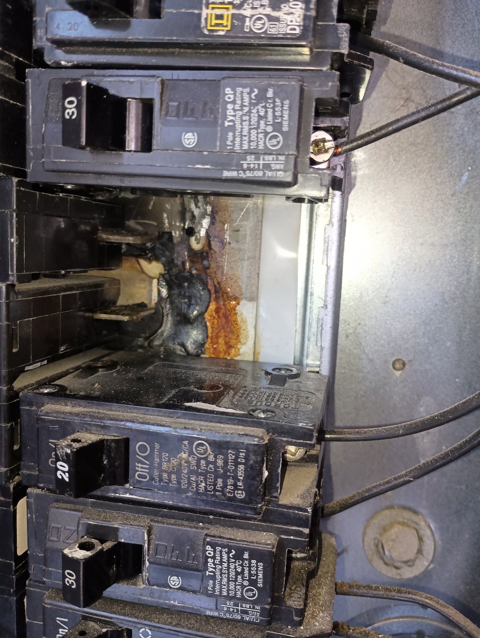 Open electrical breaker panel with several black circuit breakers and exposed wiring.