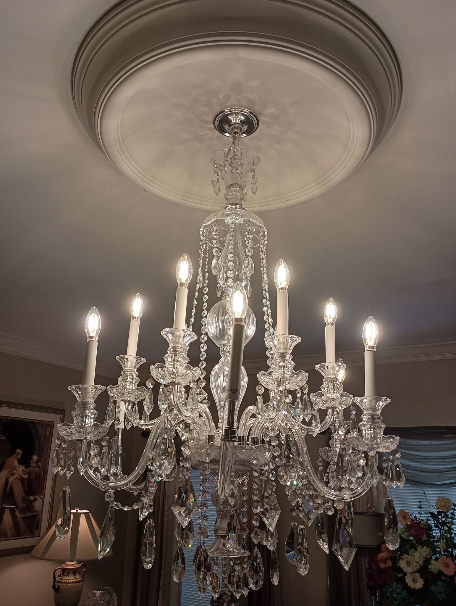 Crystal chandelier hanging from a ceiling medallion in an elegant room, with lit candle bulbs.