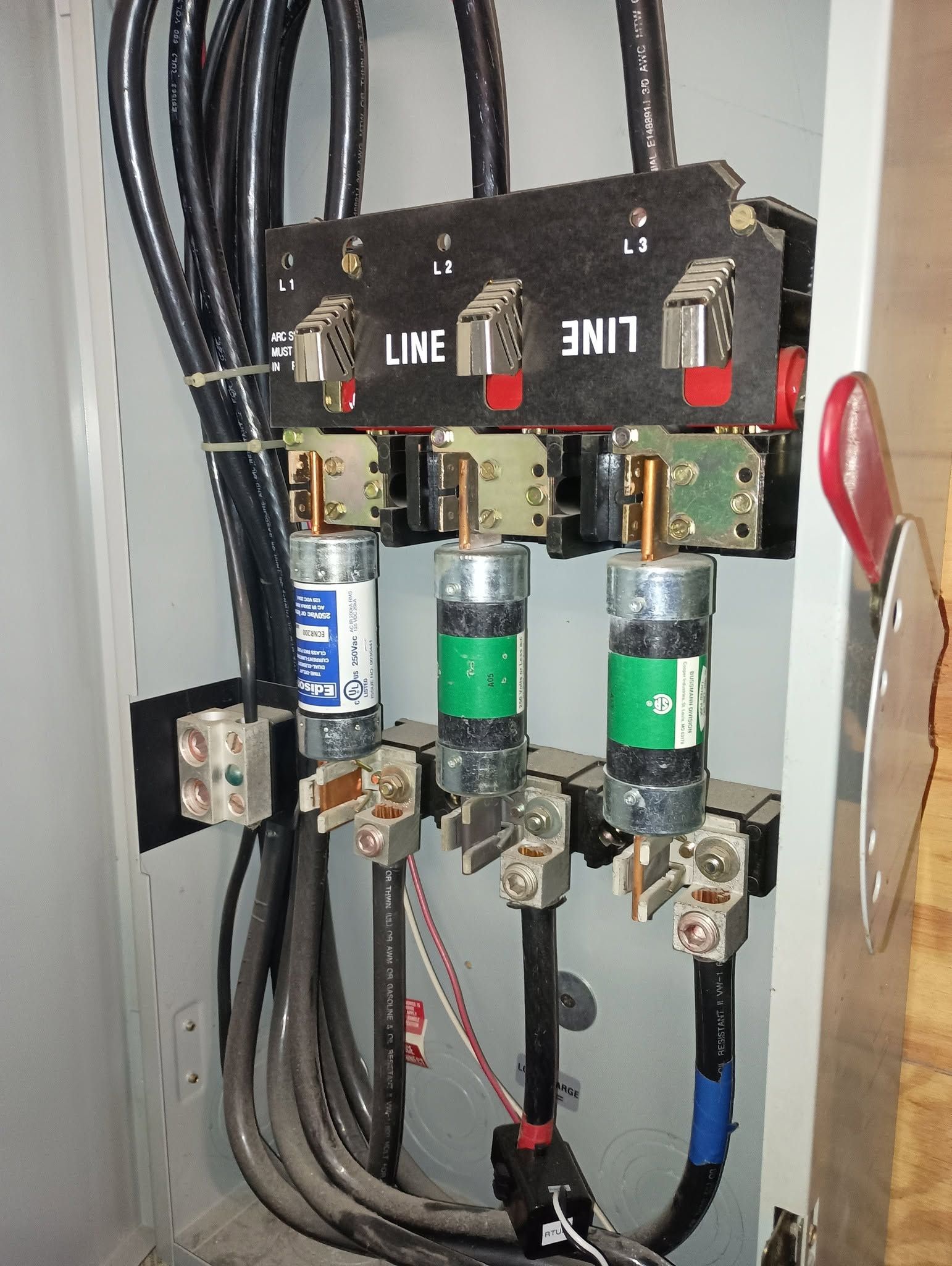 Electrical panel with three fuse holders and thick black wires inside a metal cabinet