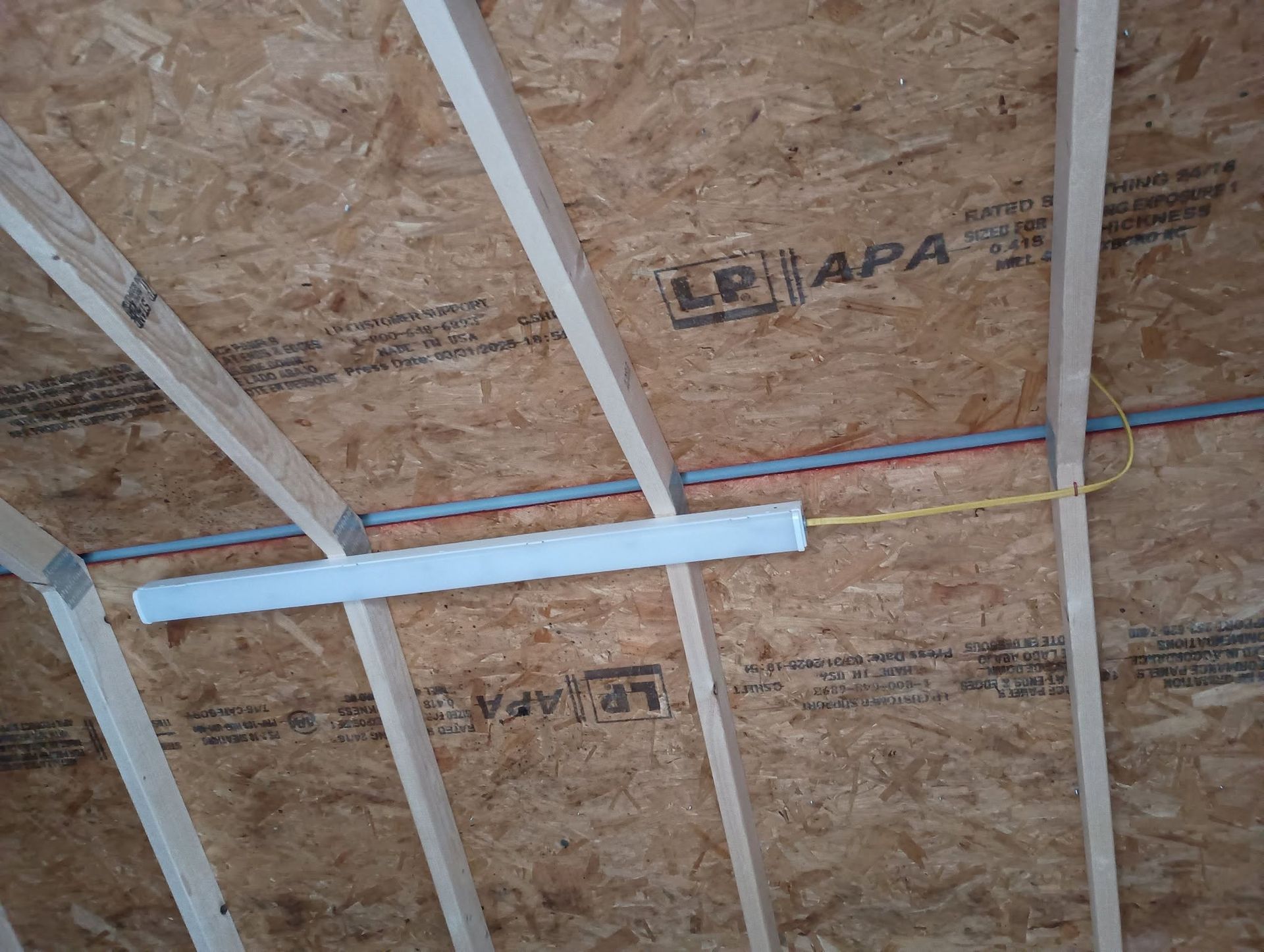 Ceiling framing with OSB sheathing and white crossbars, plus exposed blue and yellow wires.