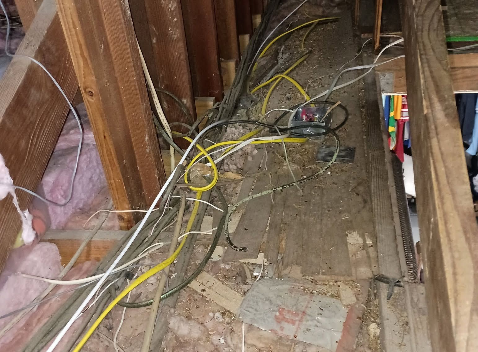 Cluttered attic crawlspace with exposed wiring, wooden beams, insulation, and debris on the floor