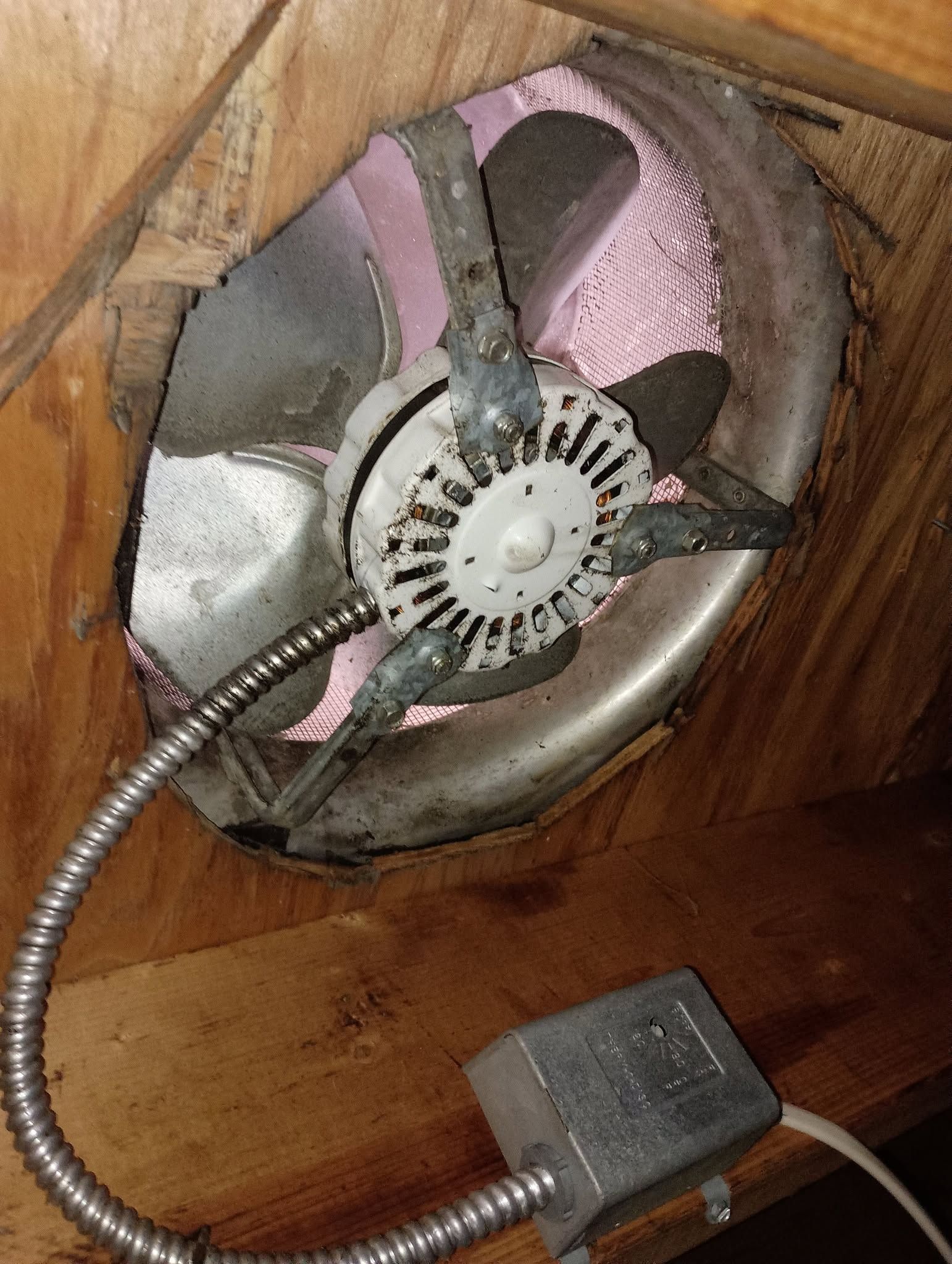 Broken ceiling fan with exposed wiring mounted in a wooden opening, connected to a small control box.