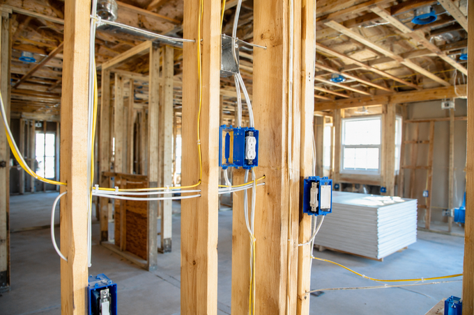 Interior of a framed house under construction with exposed wood studs, wiring, and stacked drywall panels