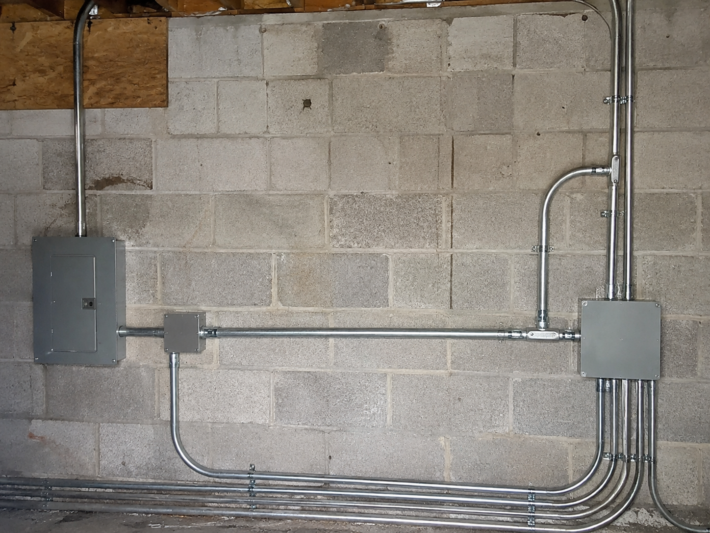 Electrical conduit and junction boxes mounted on a cinder block wall in a utility room.