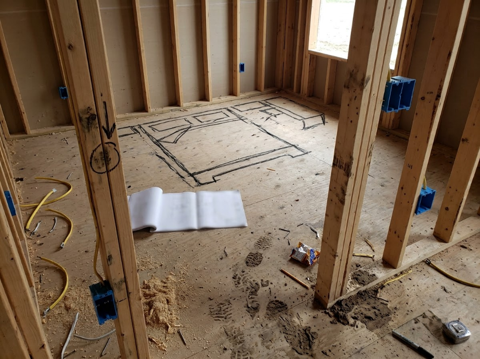 Framed house interior under construction with exposed studs, wiring, and tools on the floor.