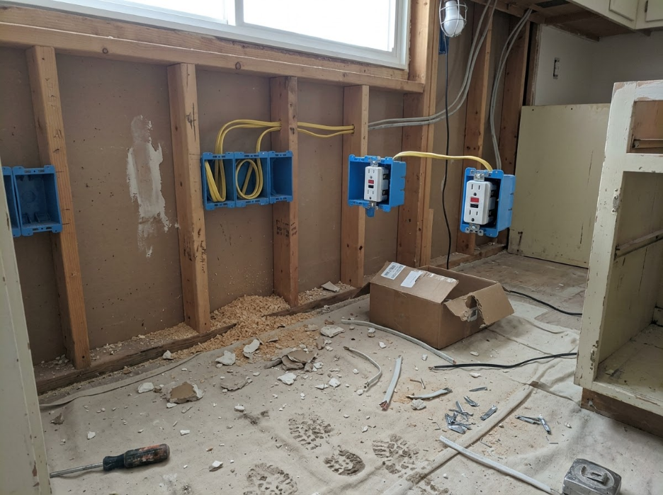 Unfinished room with exposed wall studs, blue electrical boxes, debris on the floor, and a window above.