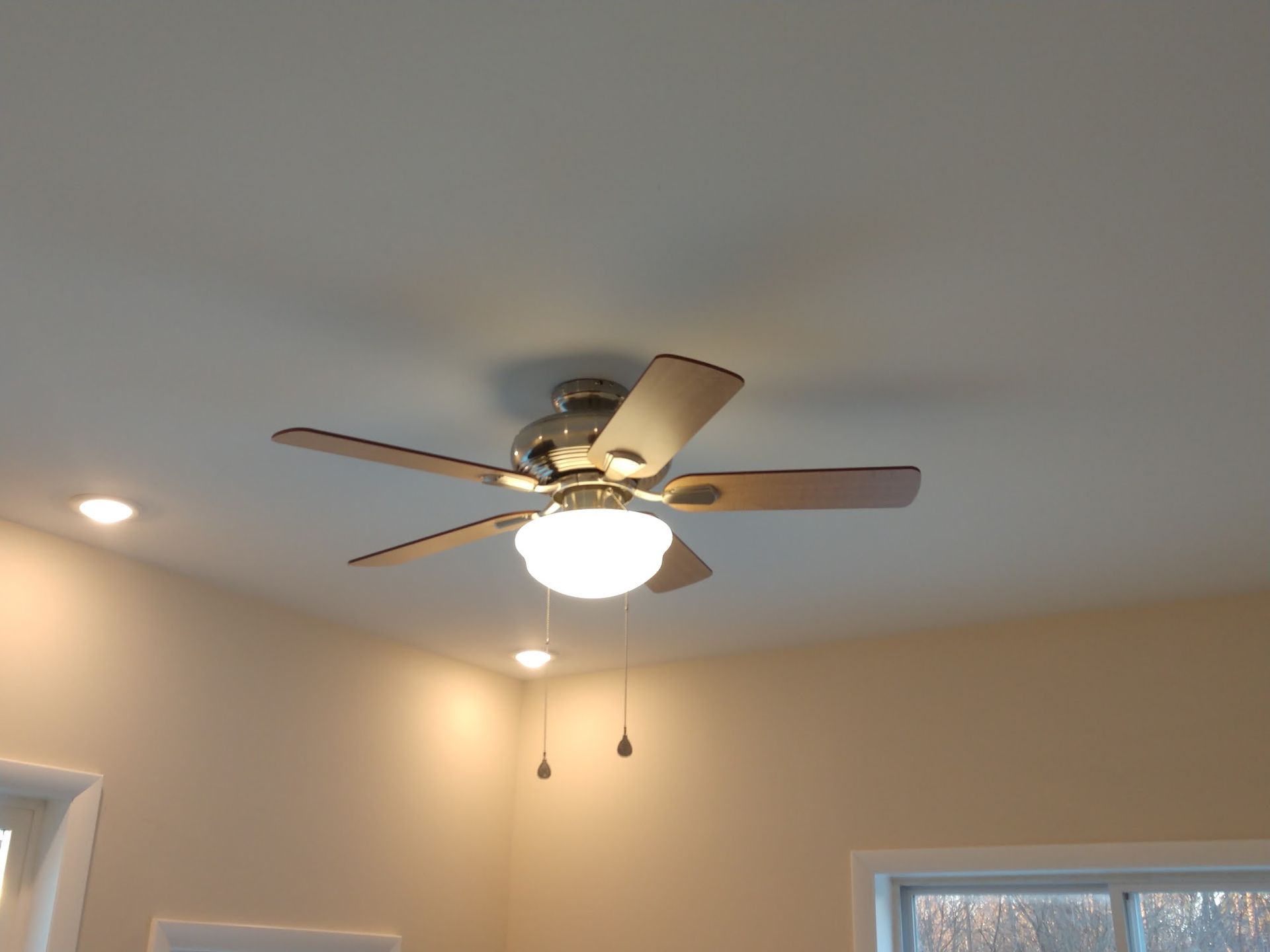 Ceiling fan with light on a beige ceiling in a room with recessed lights and windows