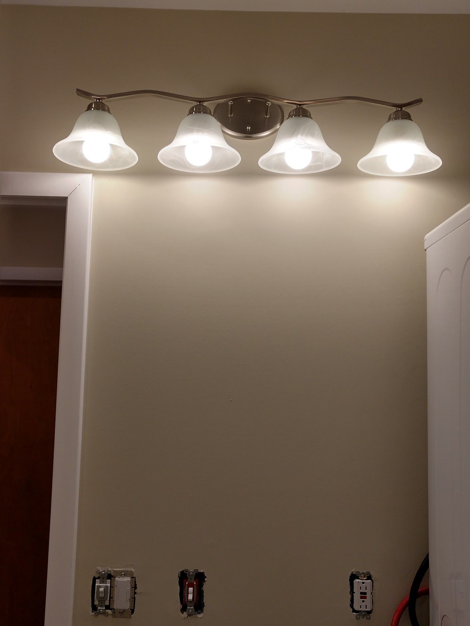 Four-bulb vanity light glowing above a beige wall, with outlets below.