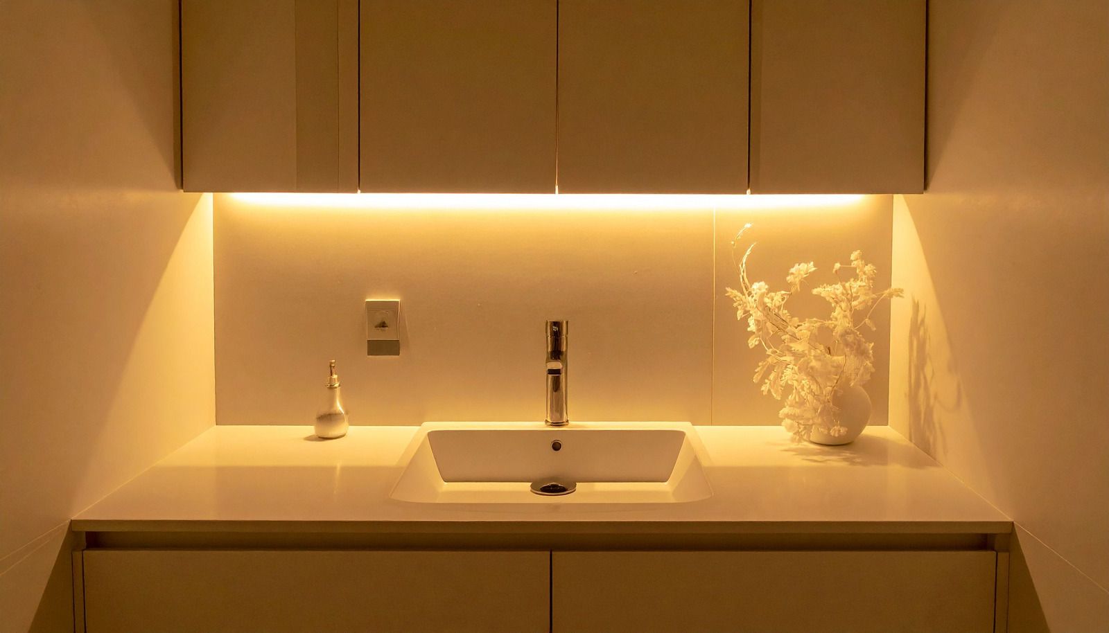 Minimalist bathroom vanity with warm under-cabinet lighting, sink, faucet, and soap dispenser on a counter.