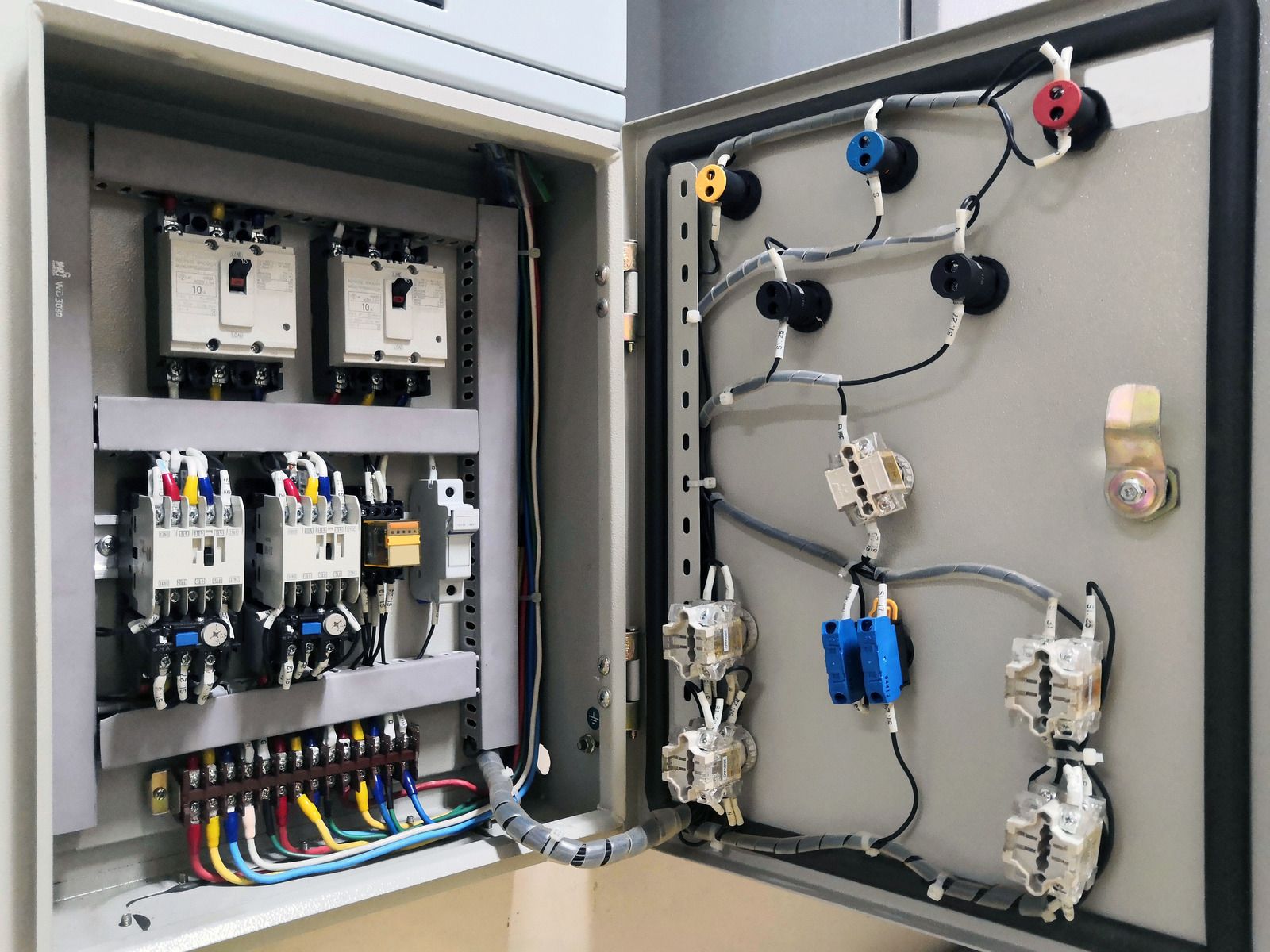 Open electrical panel in a wall with exposed components and conduit on a dusty floor