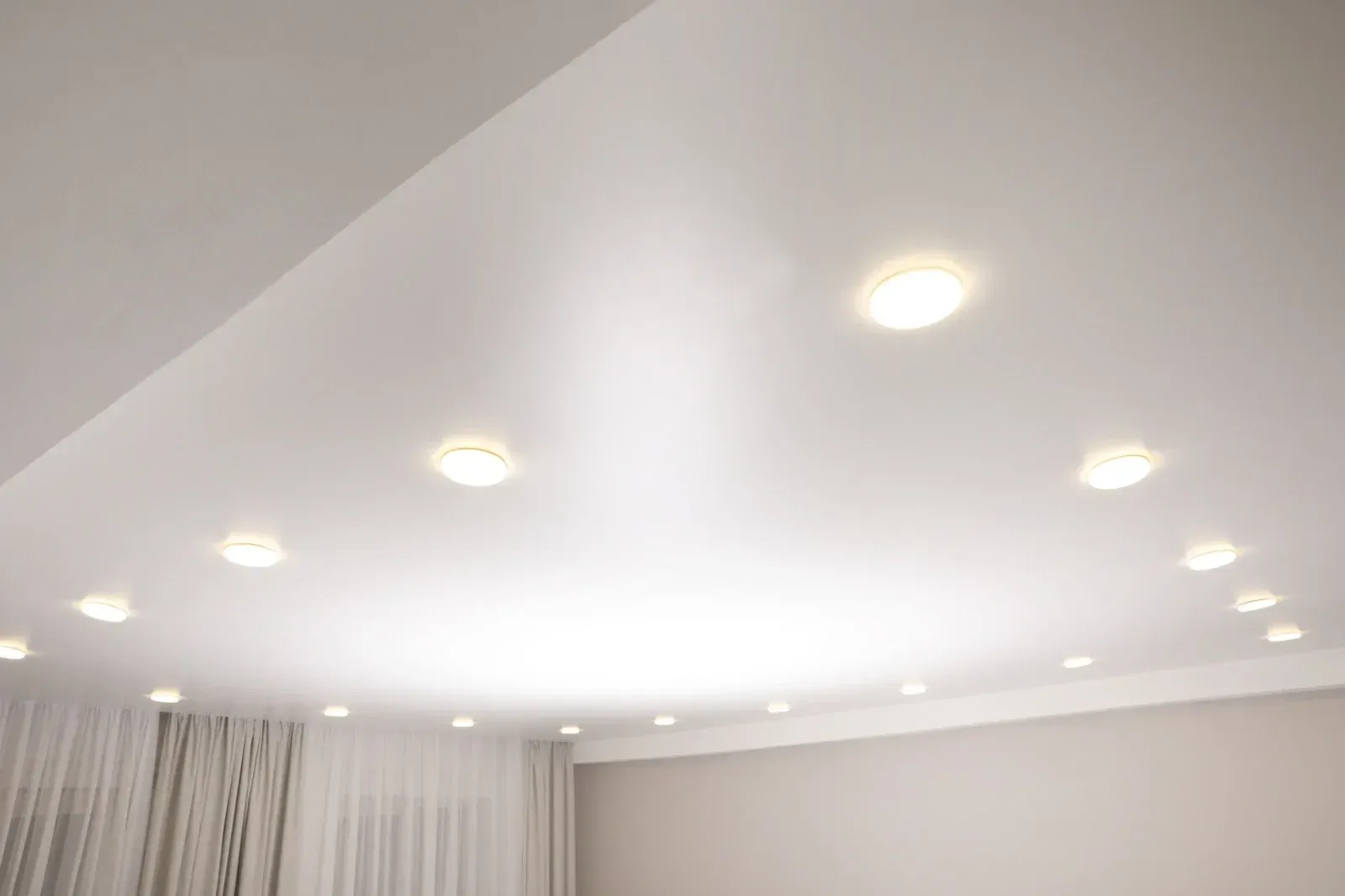 Bright white ceiling with recessed lights in a modern room, with curtains visible below.