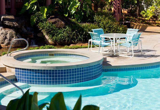 Backyard pool with circular spa, turquoise water, and white patio chairs under lush greenery