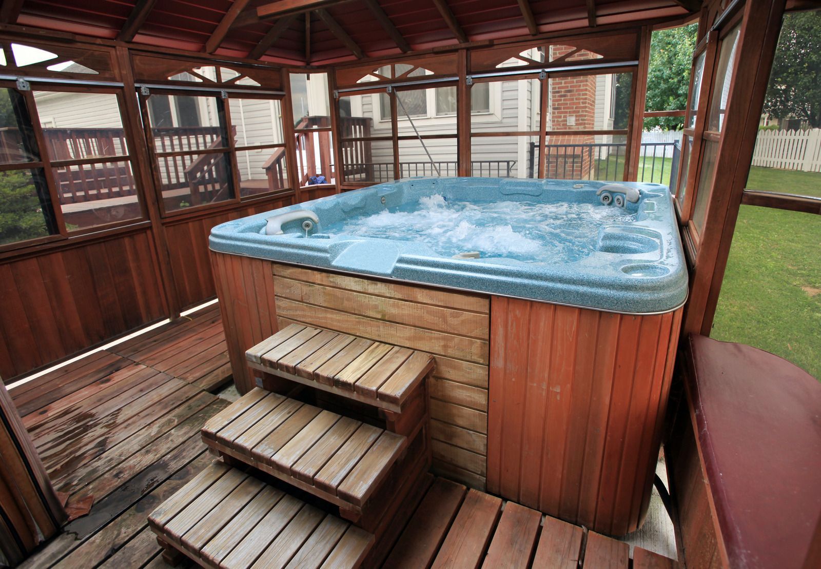 Wooden hot tub bubbling inside a covered gazebo with steps and bench seating