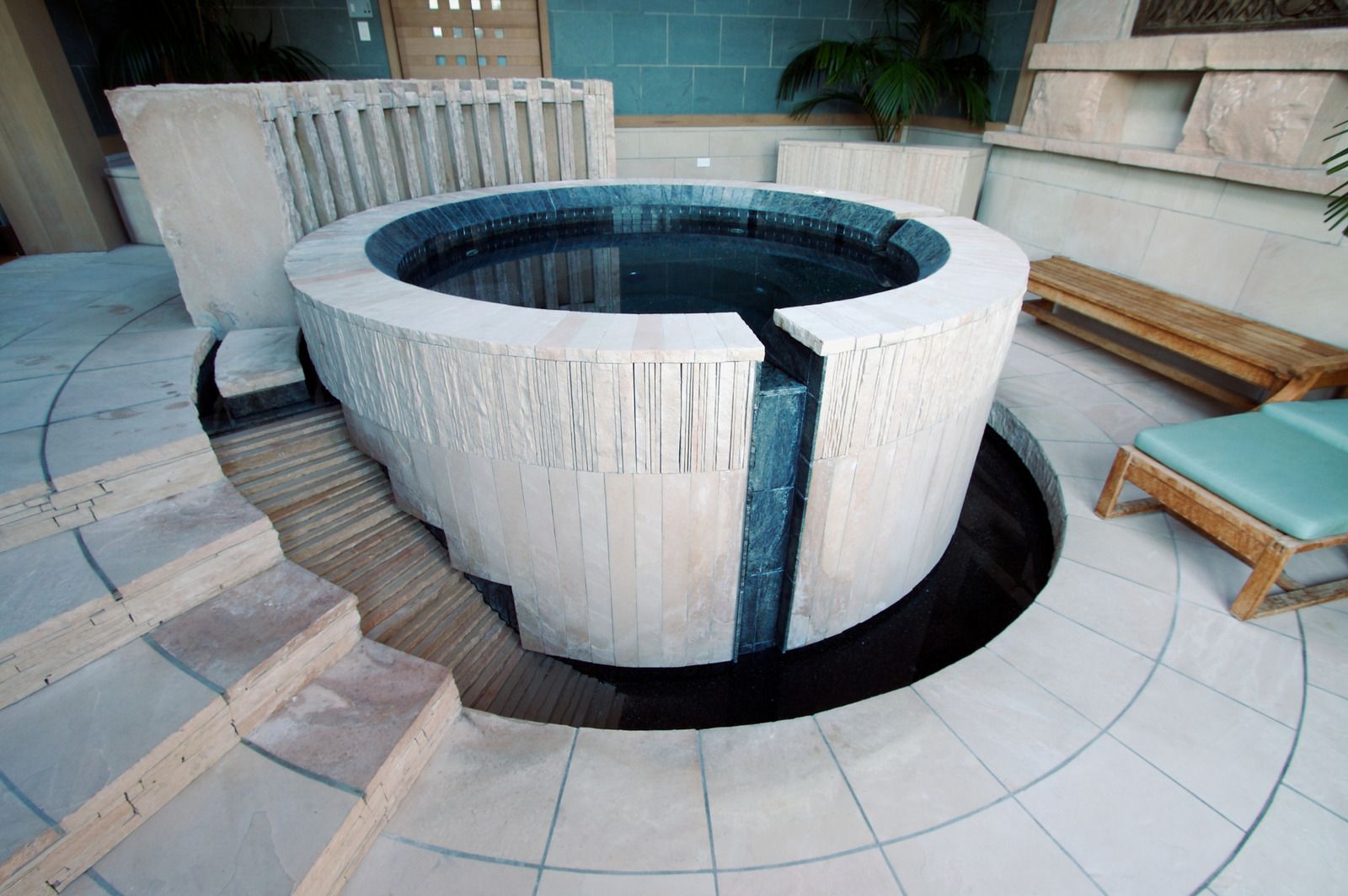 Outdoor circular white hot tub with dark water, built into a tiled patio with steps and benches nearby