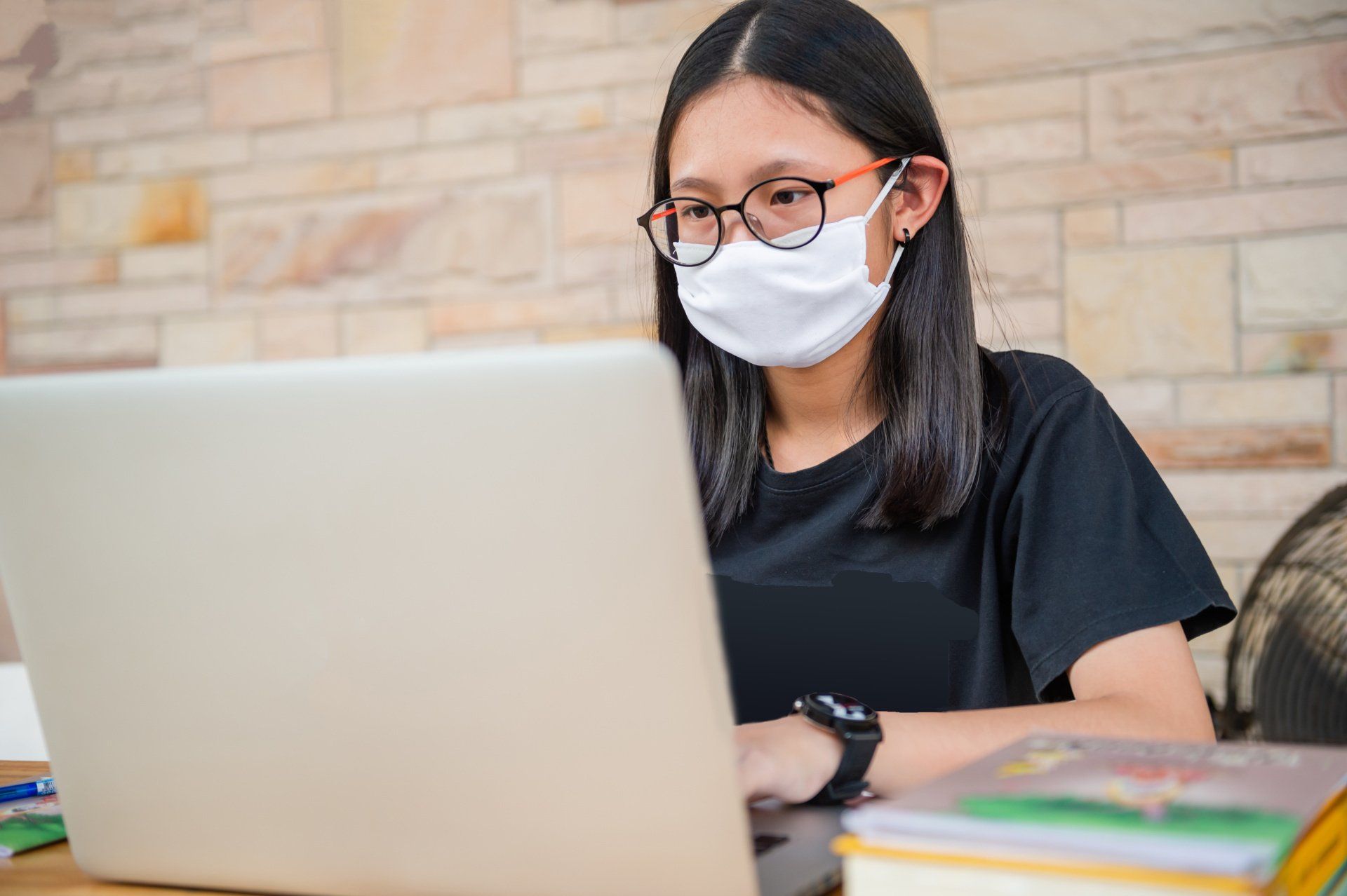 A woman wearing a mask and glasses is using a laptop computer.