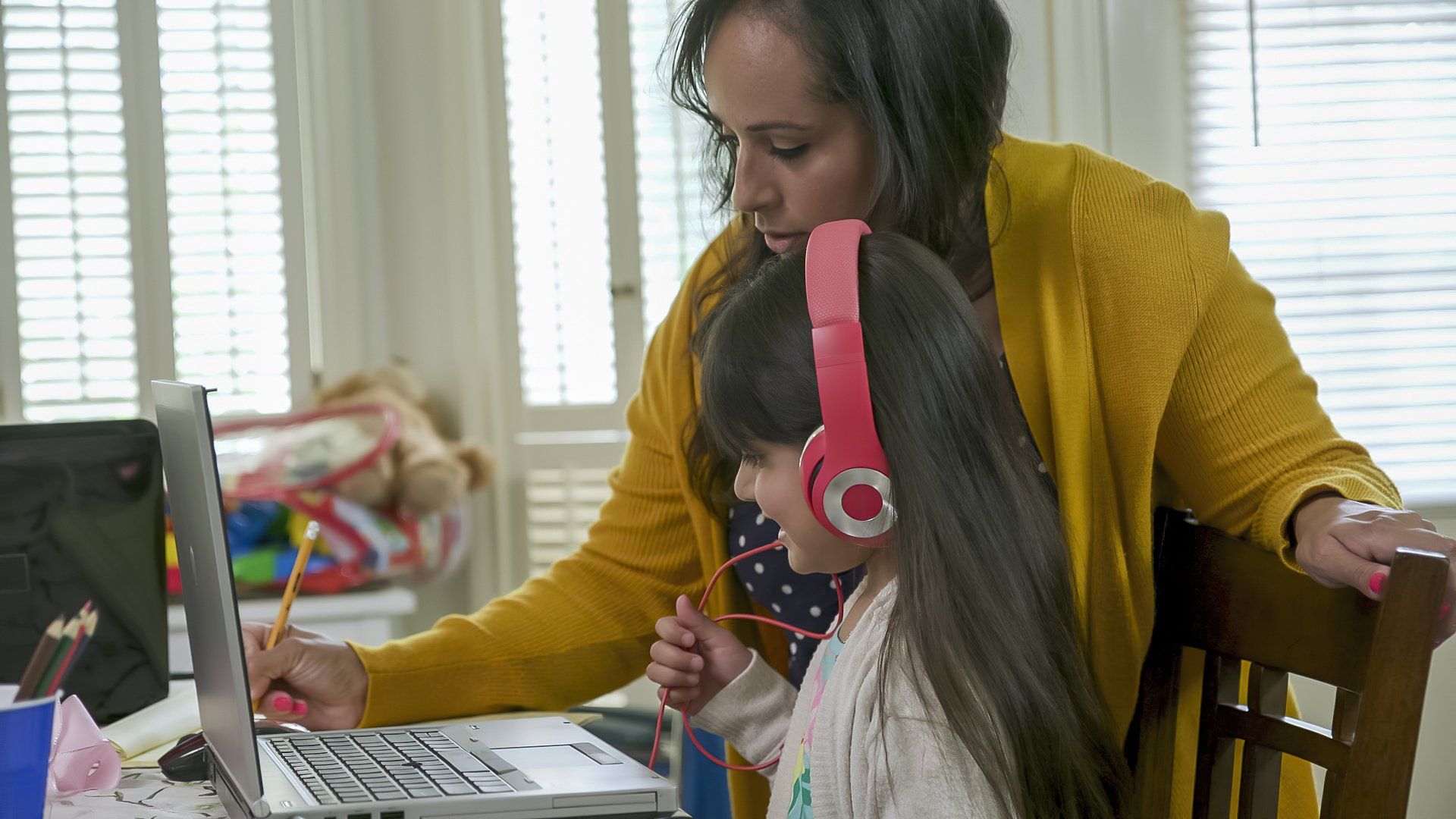 A woman is teaching a little girl how to use a laptop computer.