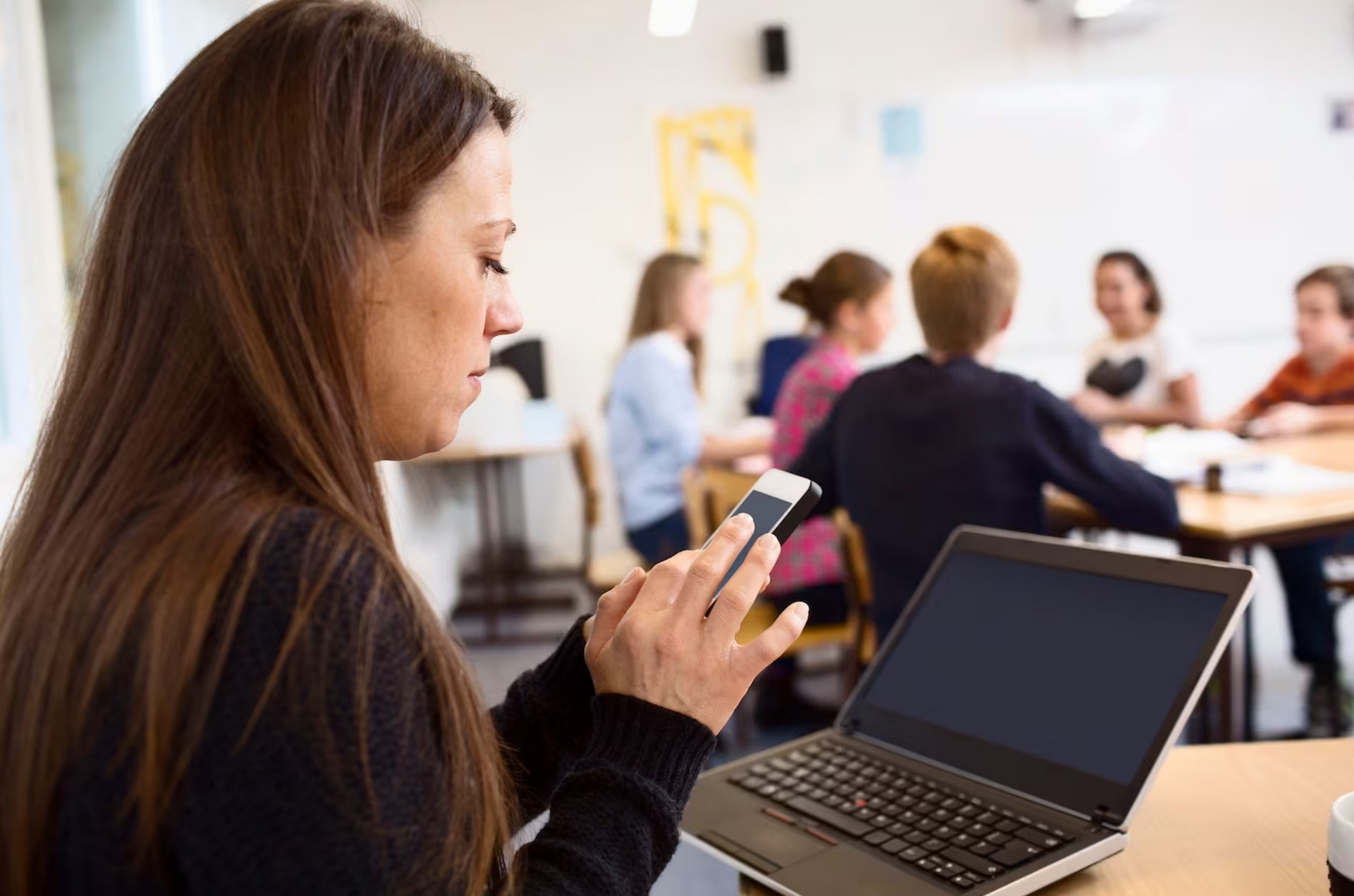 A woman is sitting at a table with a laptop and a cell phone.