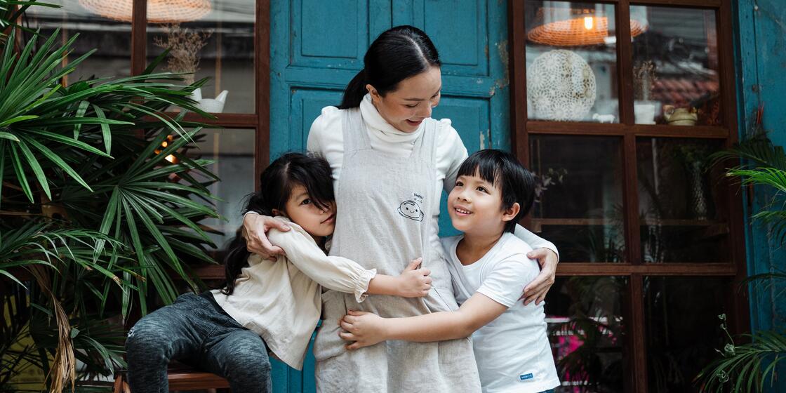 A woman is hugging two children in front of a blue door.