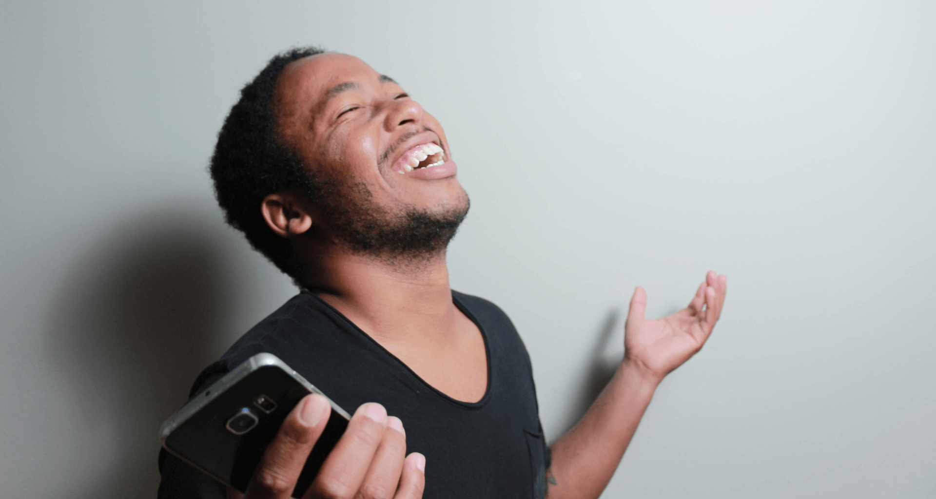 A man is laughing while holding a cell phone in his hand.