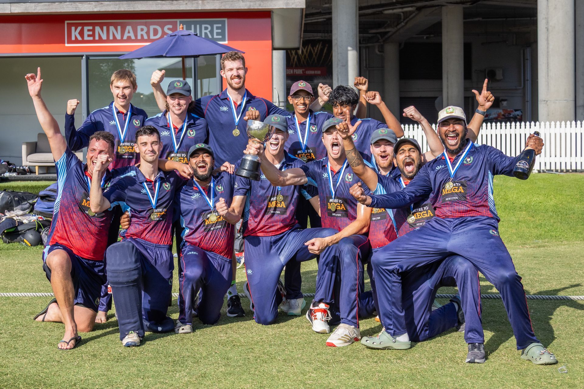 Sports team posing with medals and trophies outside a building, cheering in blue and red uniforms